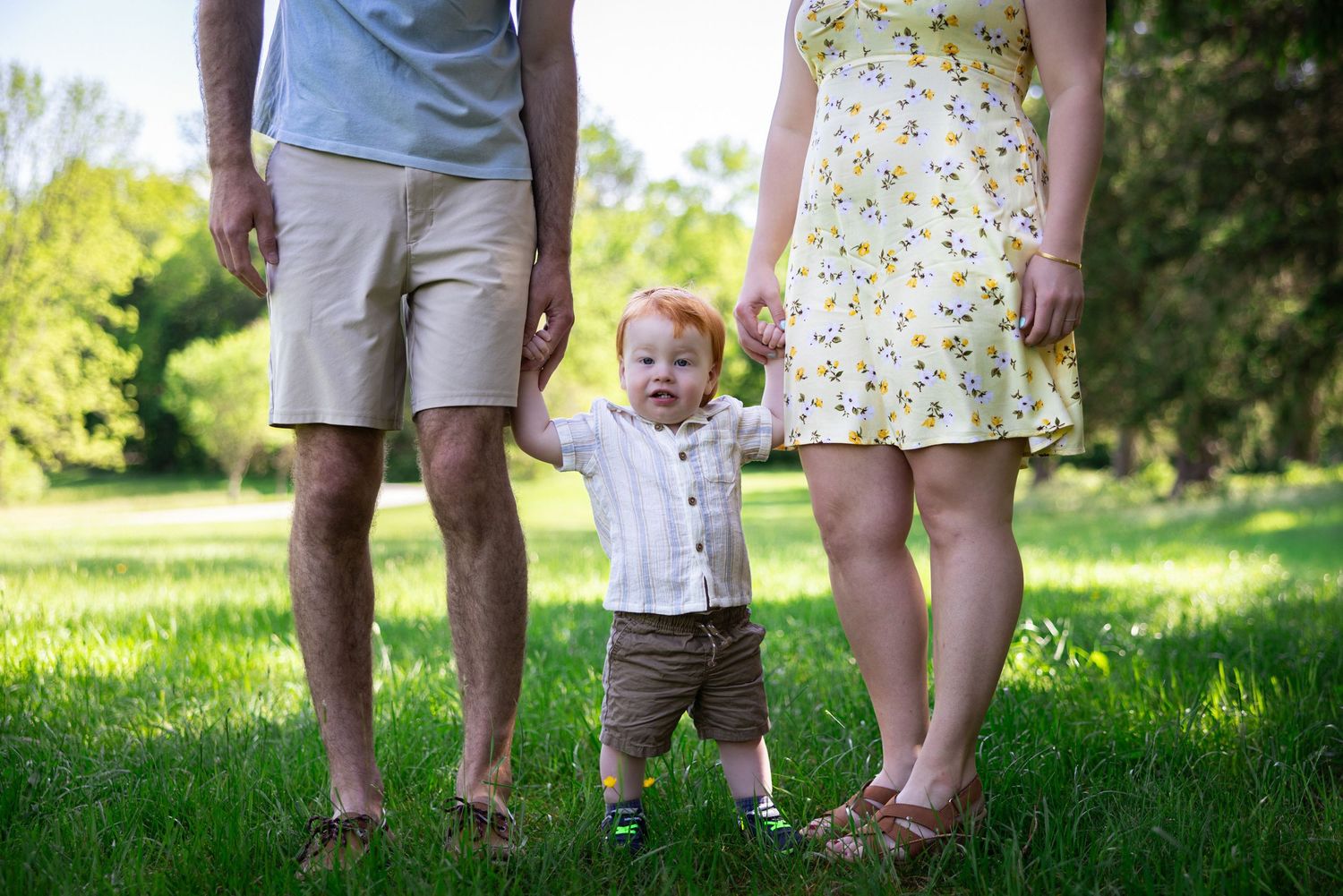 Family's feet and legs shown standing together on green grass in summer.