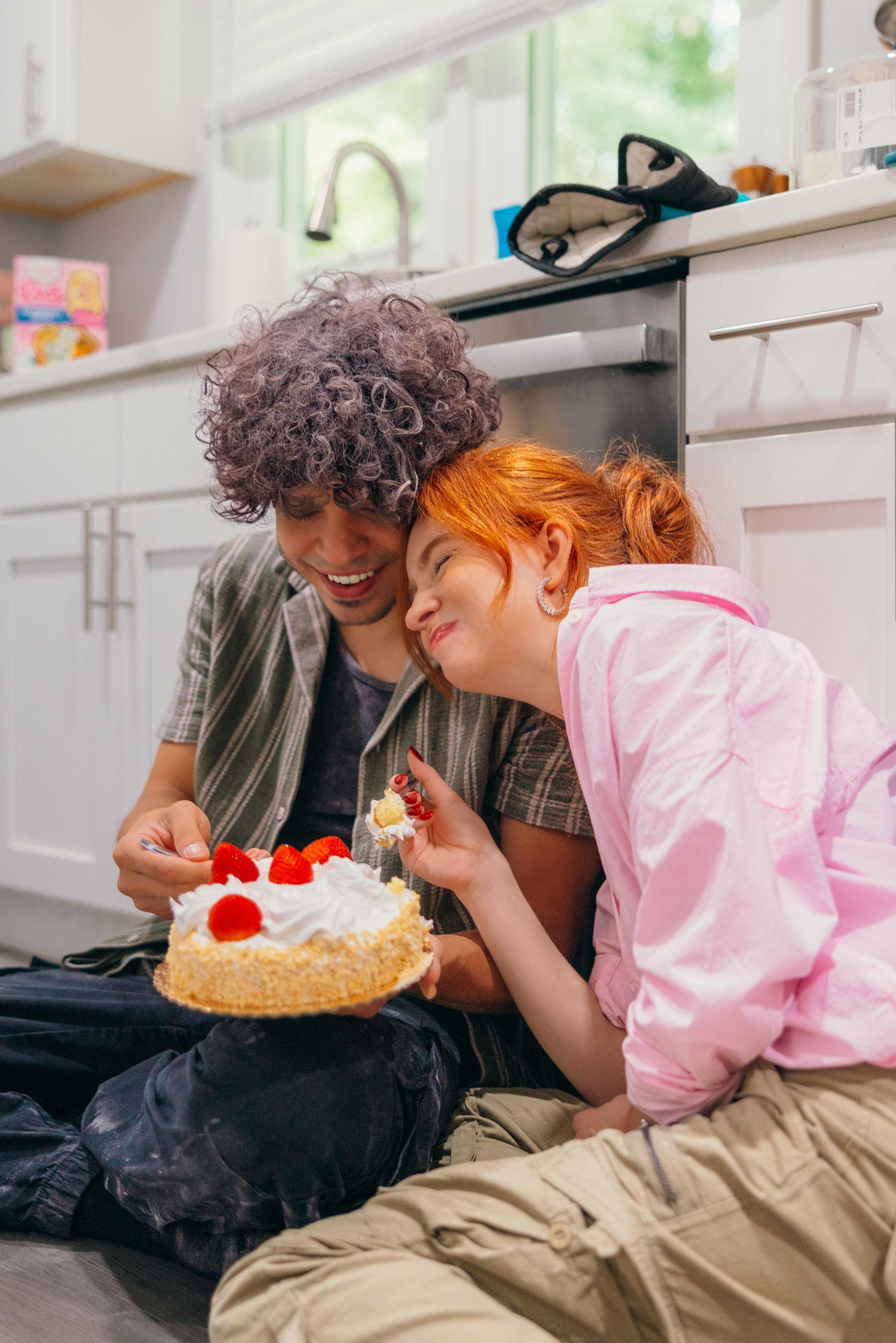 Couple sharing dessert and laughing while relaxing on a couch in a casual indoor setting.