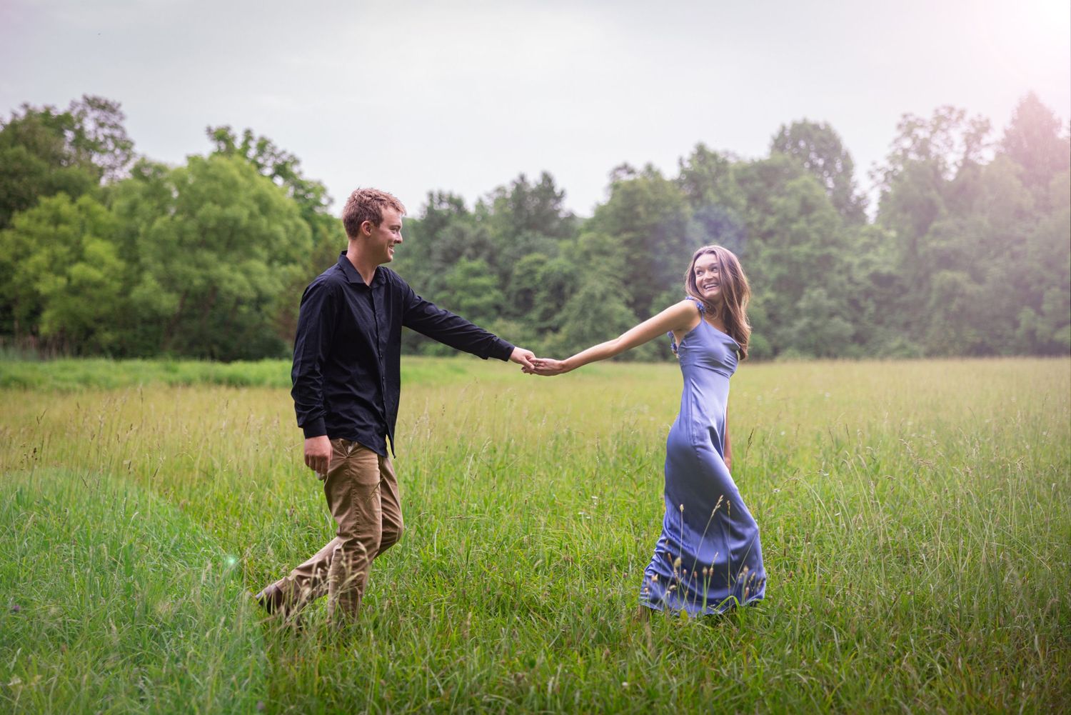 Couple walking and playing in a sunlit meadow during golden hour.