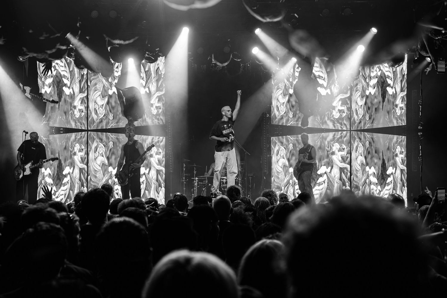 Black and white concert photo of a band performing on stage with dramatic lighting and a large crowd.