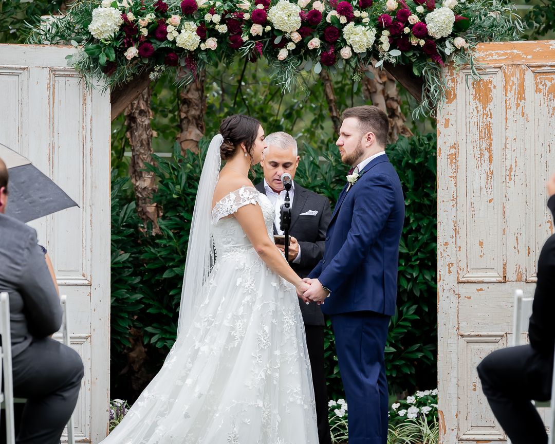 A wedding ceremony backdrop featuring vintage doors decorated with pink and white floral arrangements.