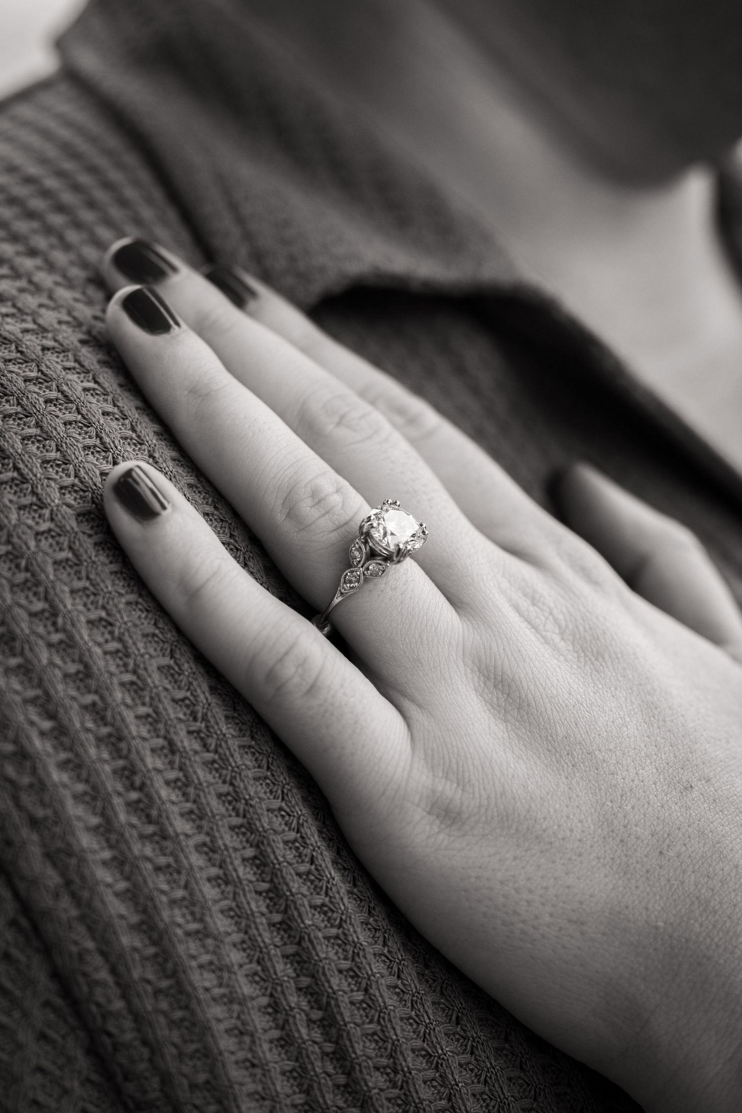 Close-up of engagement ring on hand against textured gray fabric background.