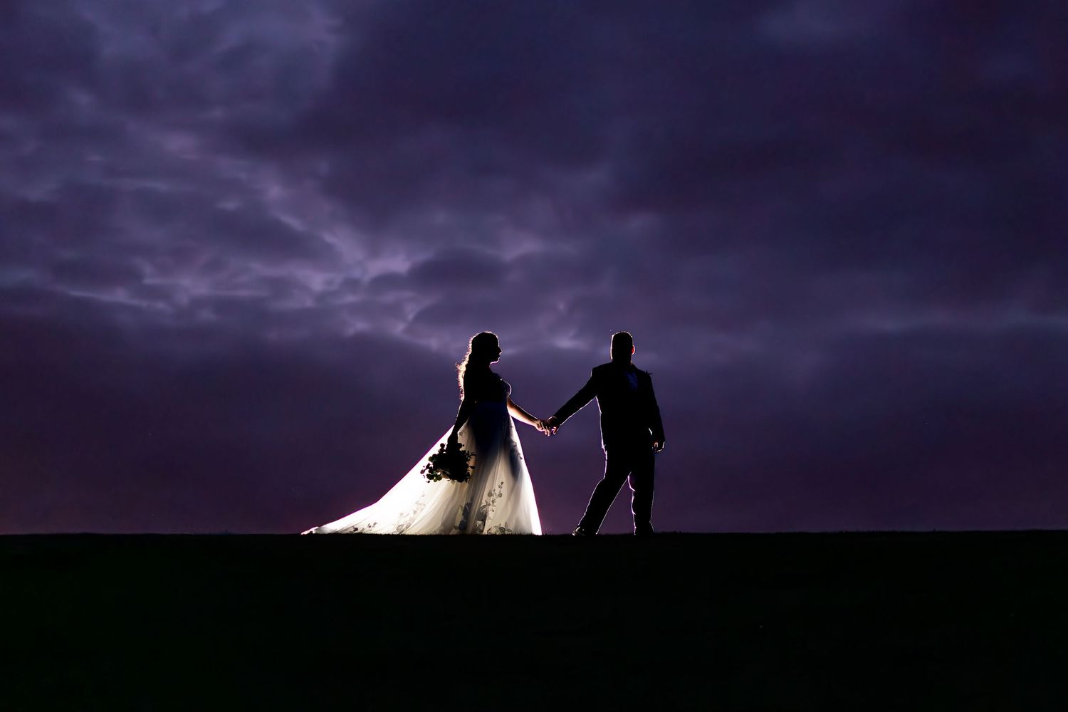 Silhouettes of a wedding couple against a dramatic purple sunset sky.