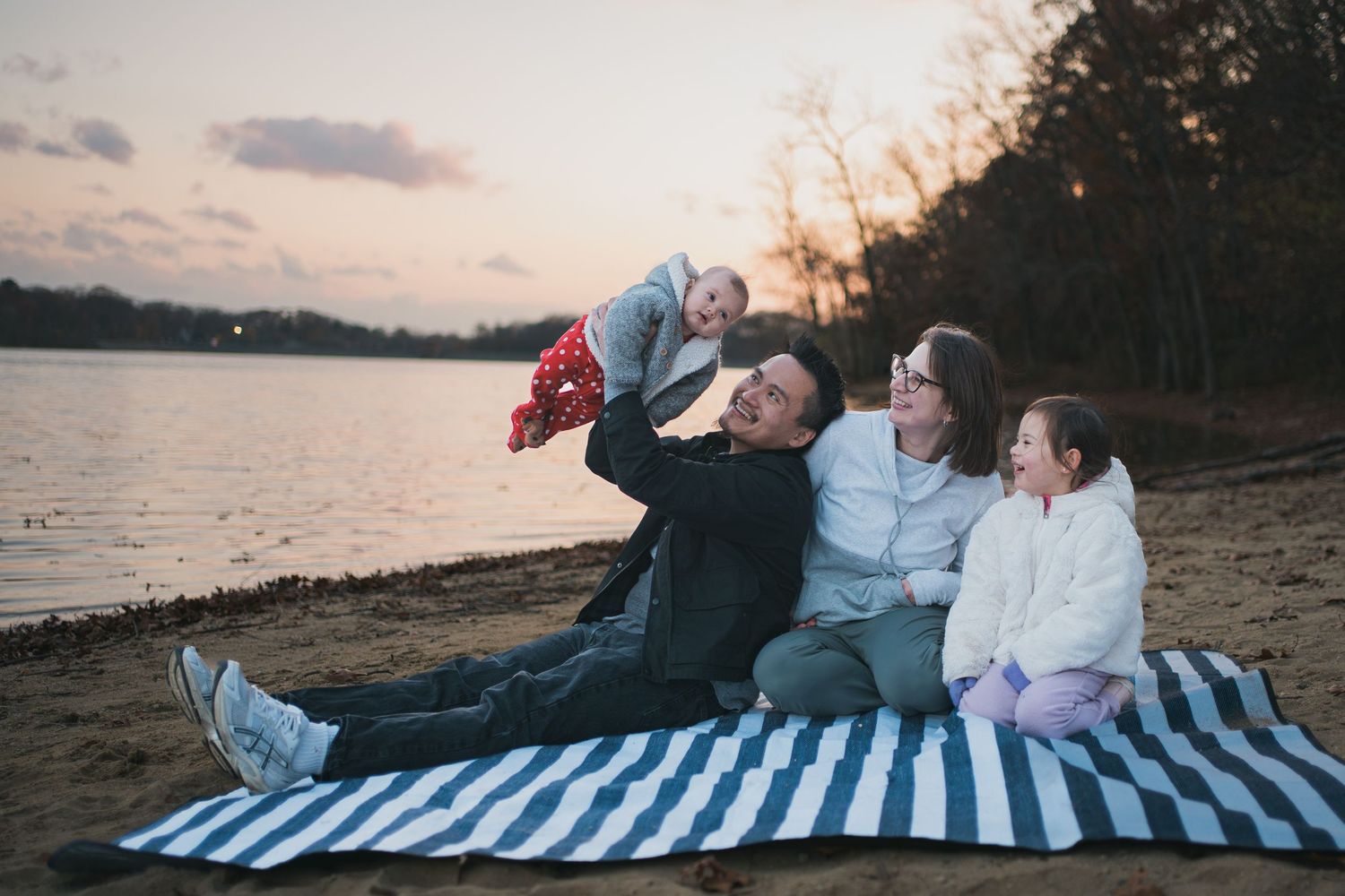 Family relaxing on a striped blanket at the beach during sunset.
