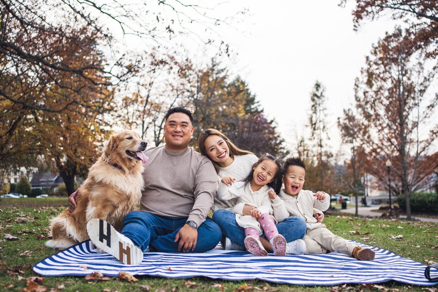 Family and dog relaxing on blanket during autumn outdoor photoshoot.