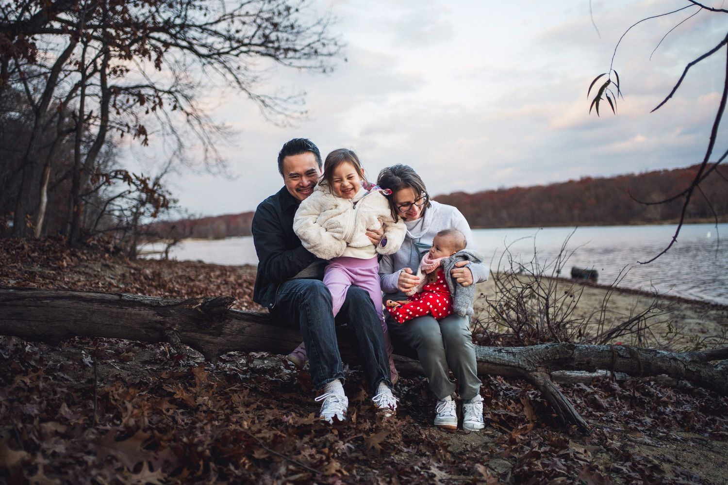 Family sitting together on fallen tree trunk by lake during sunset.