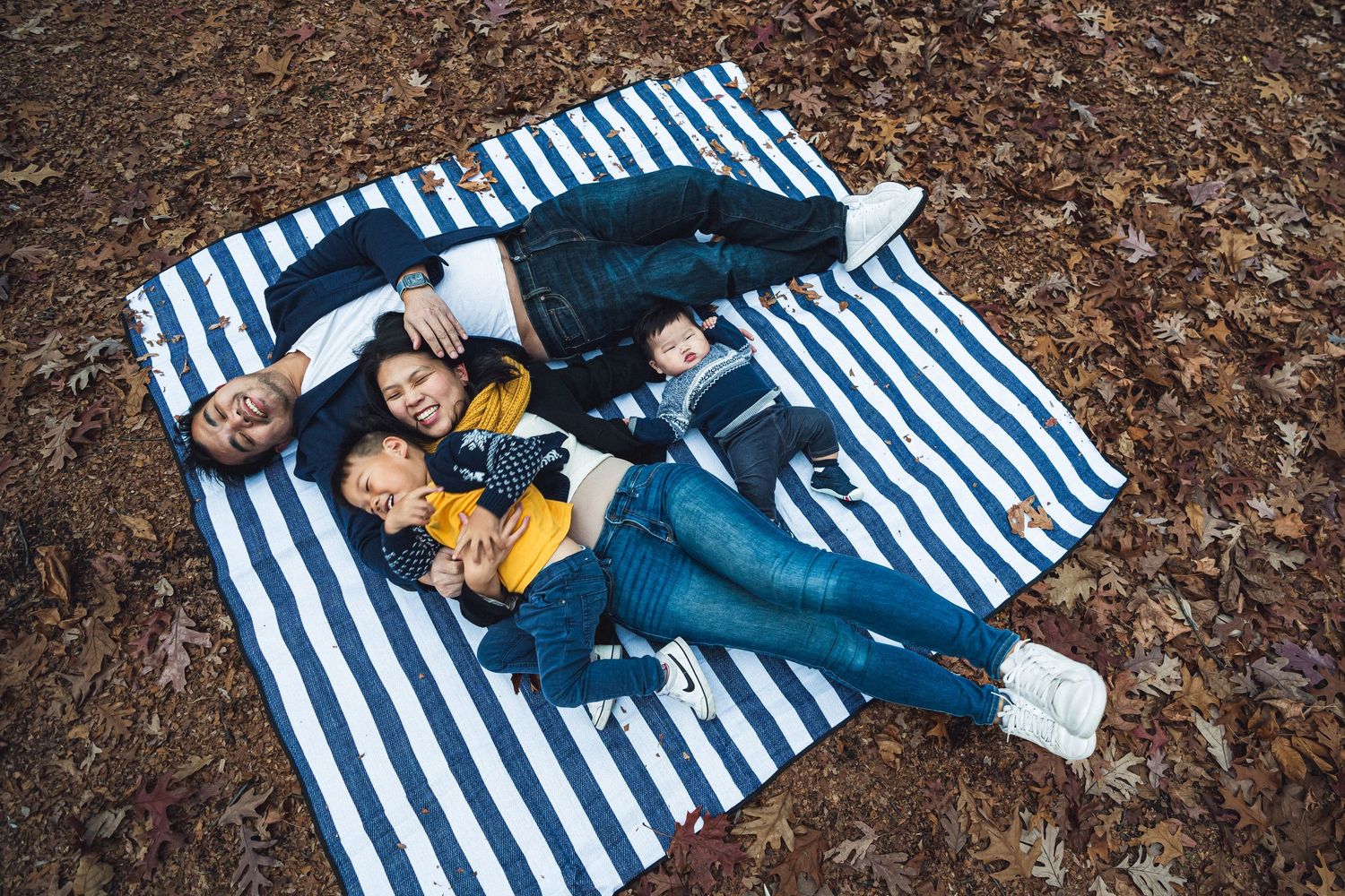 People lounging on a blue and white striped blanket among scattered leaves in Hempstead Lake