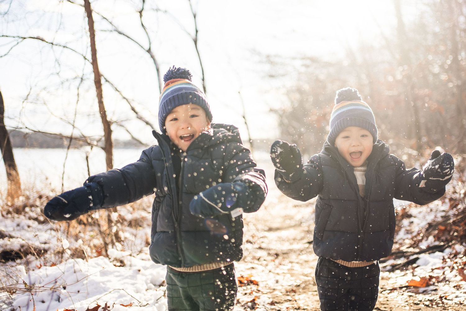 Two kids having fun throwing snow on a bright winter afternoon.