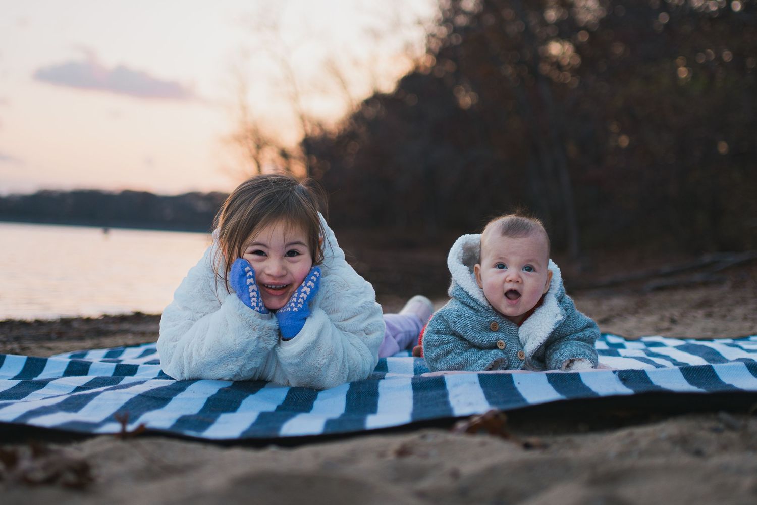 People lying on a blue and white striped blanket by the water at sunset.