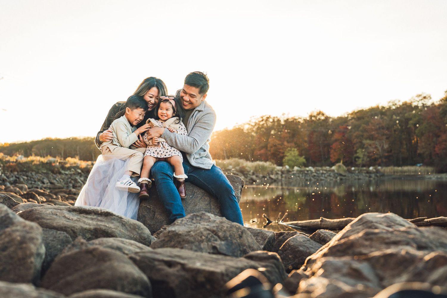 Family relaxing on rocky coastline during golden hour sunset.