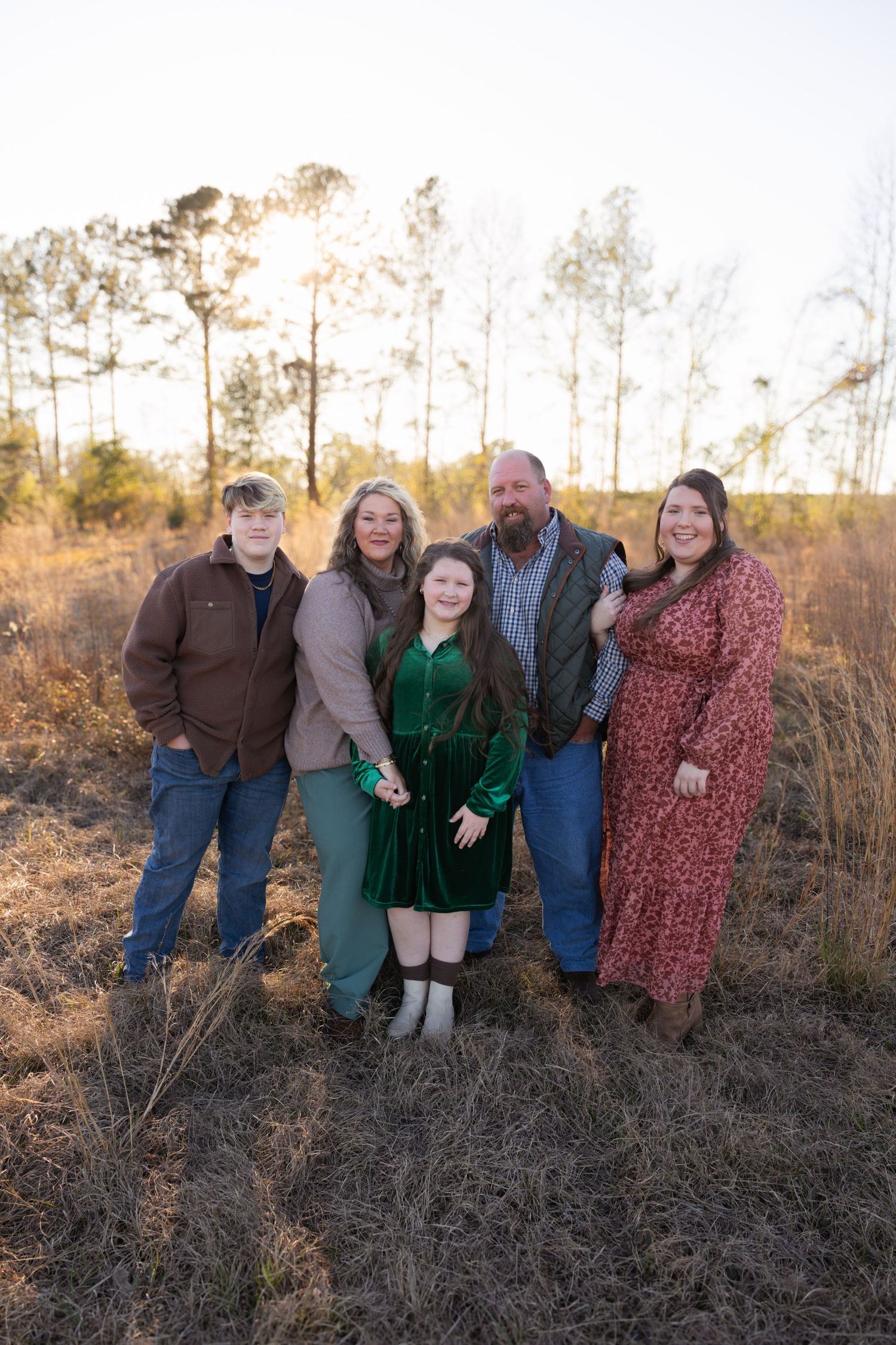 Family of five posing together in a golden field during sunset, wearing coordinated fall outfits.