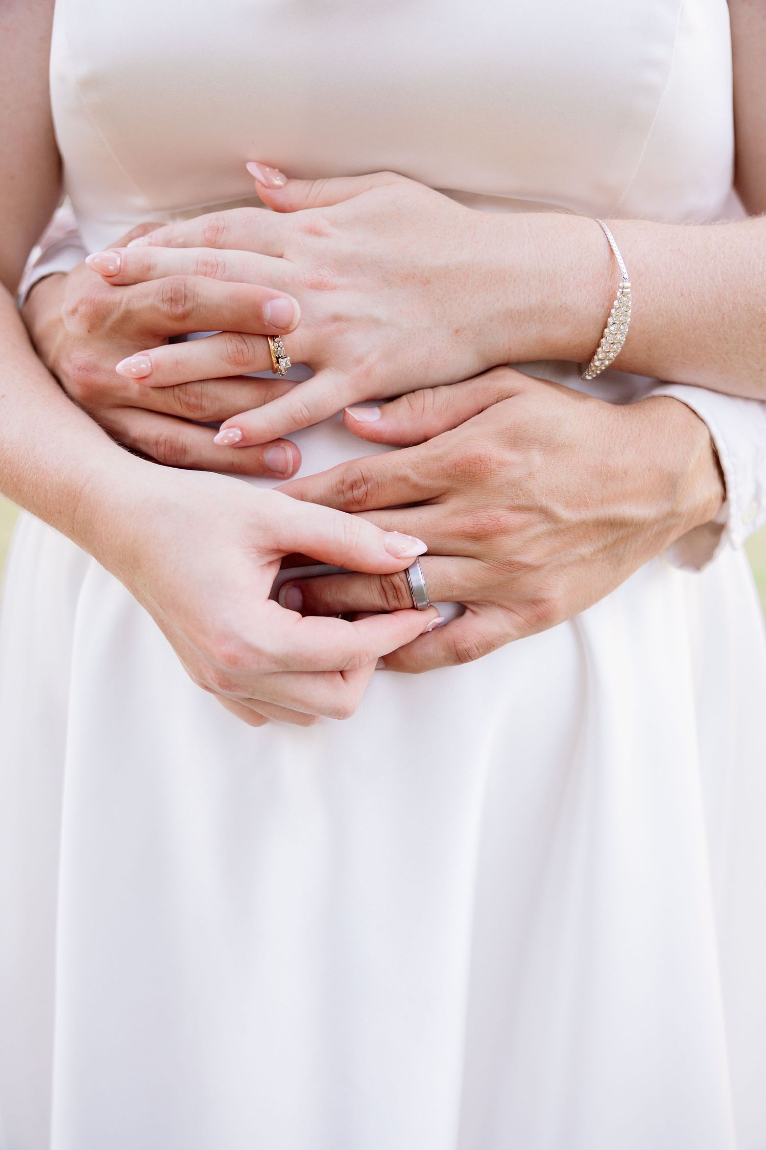 Newlywed couple holding hands showing wedding rings, bride in white dress with pearl bracelet. Wedding Photographer Alyson Williams