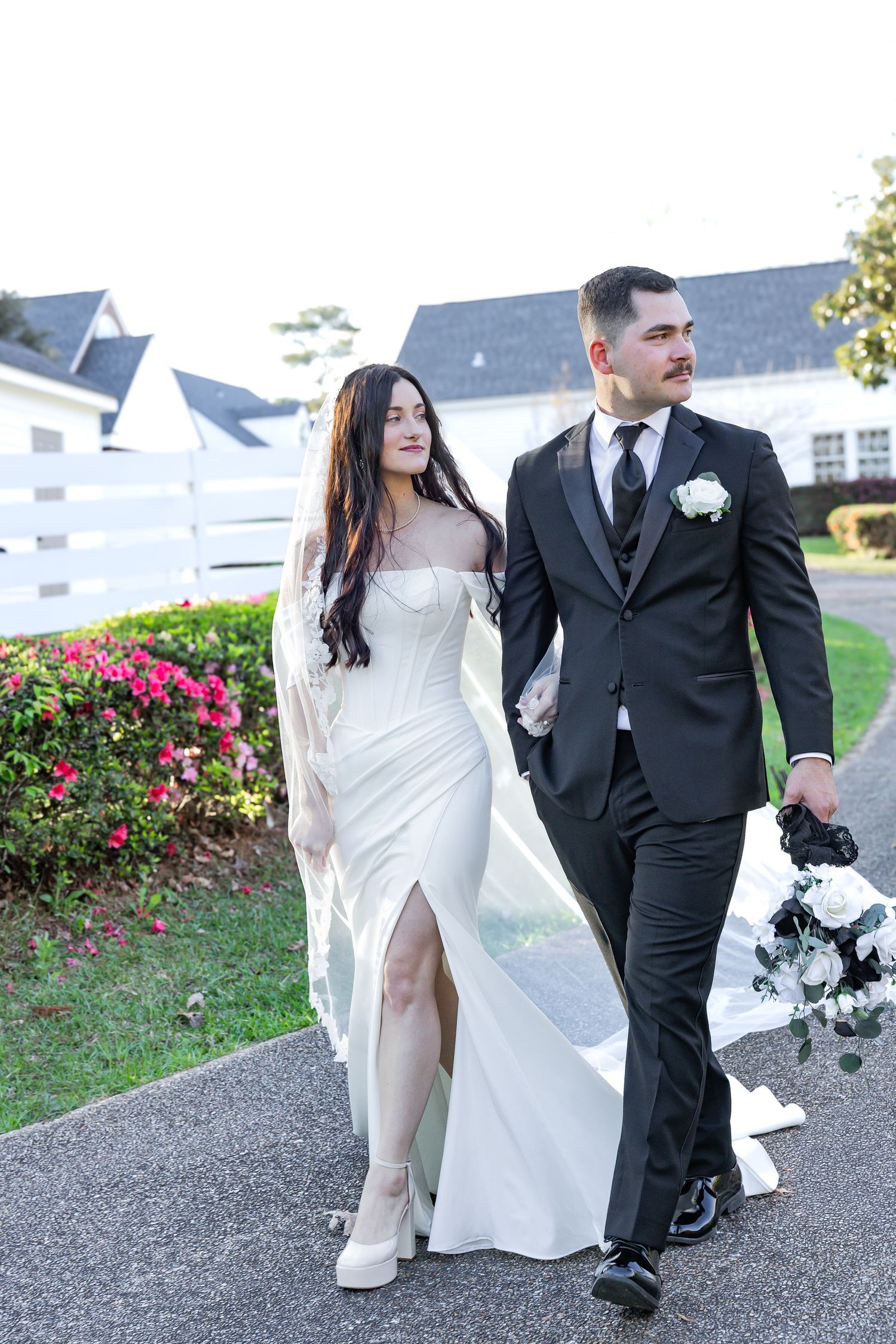 Bride in white gown and groom in black tuxedo walking hand in hand outdoors at their wedding venue.