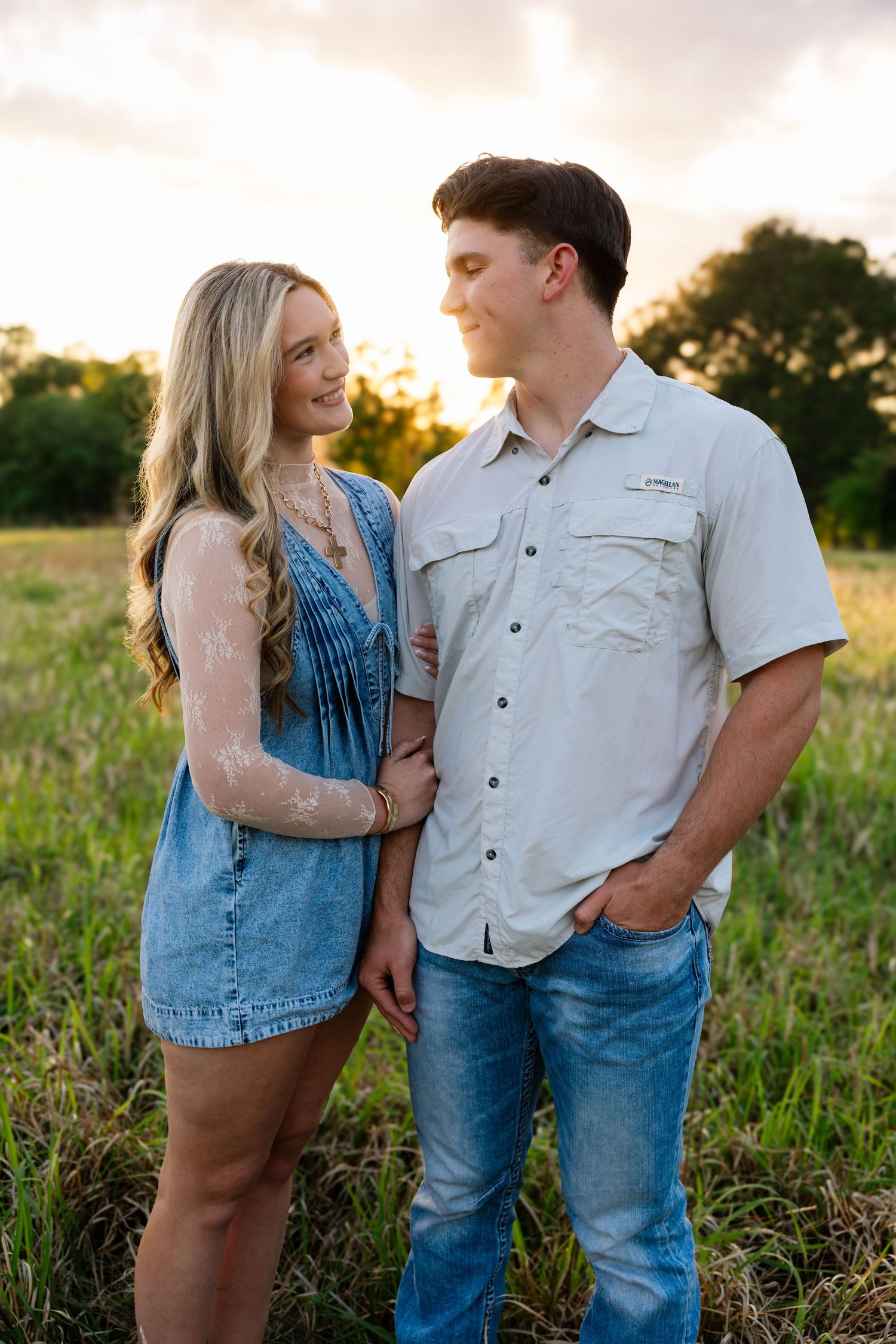 Young couple gazes at each other lovingly in green meadow during golden hour.