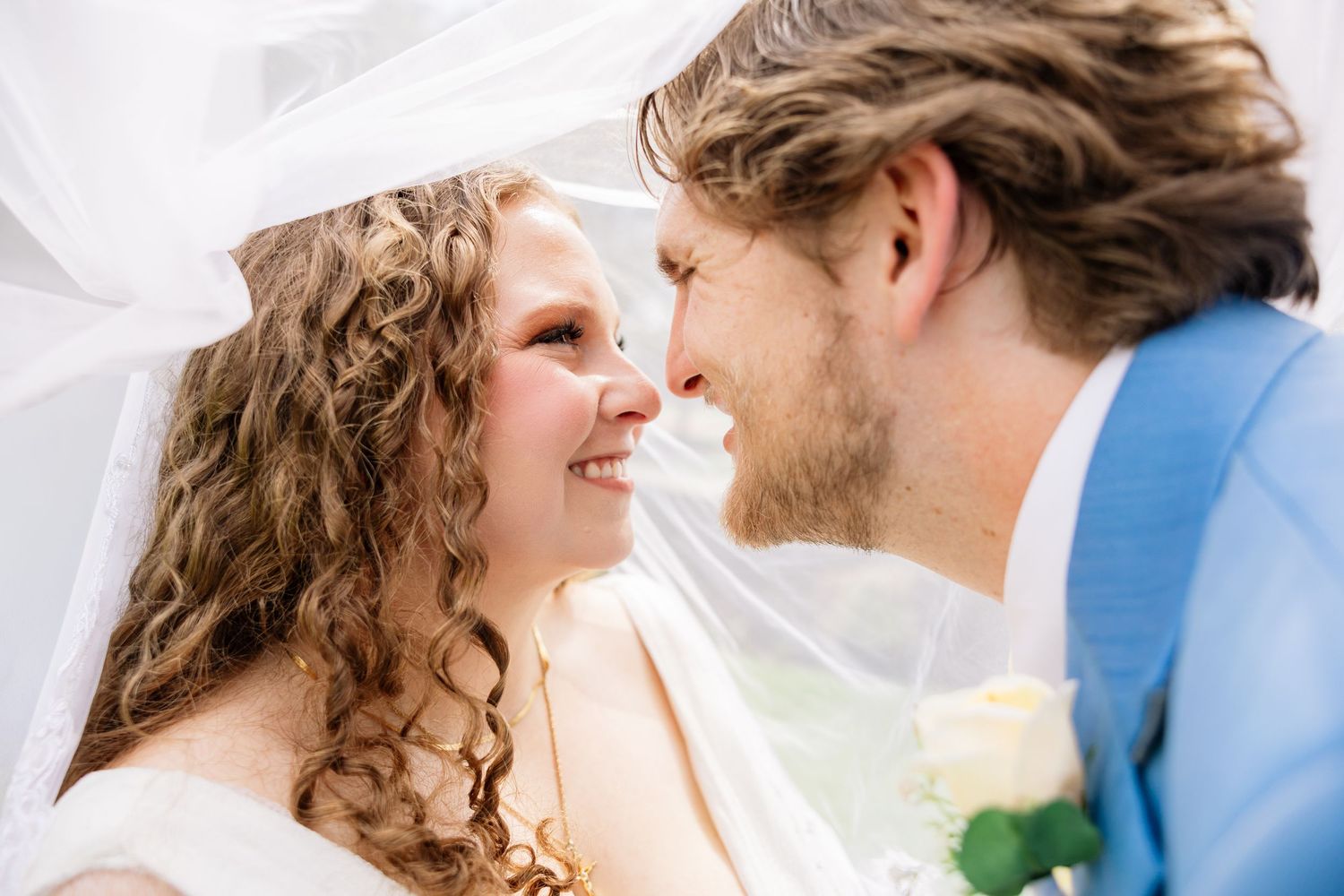 Bride and groom share a romantic moment under a wedding veil, smiling at each other on their special day.