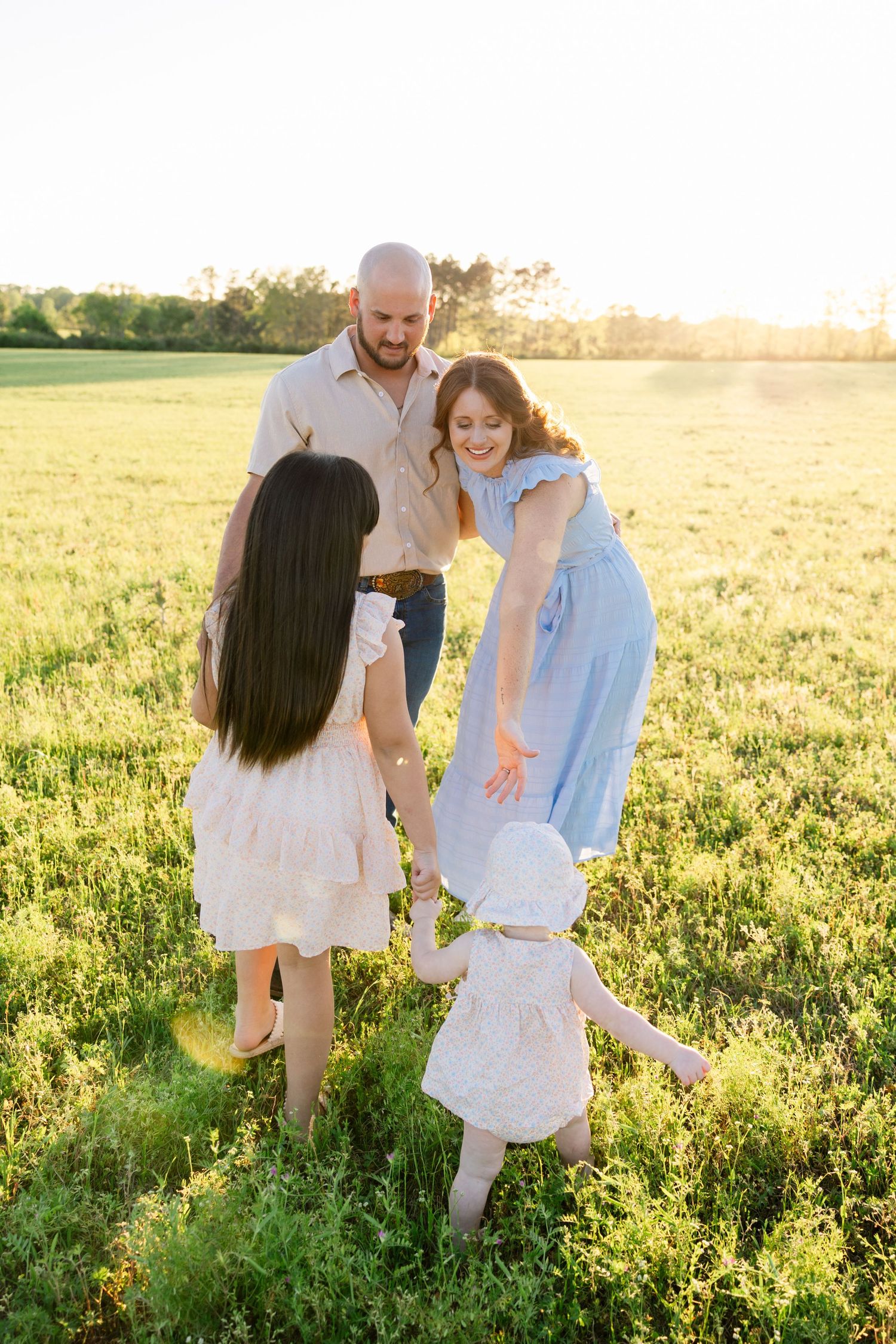 Family of four enjoying playful moment together in bright sunlit green meadow at sunset.