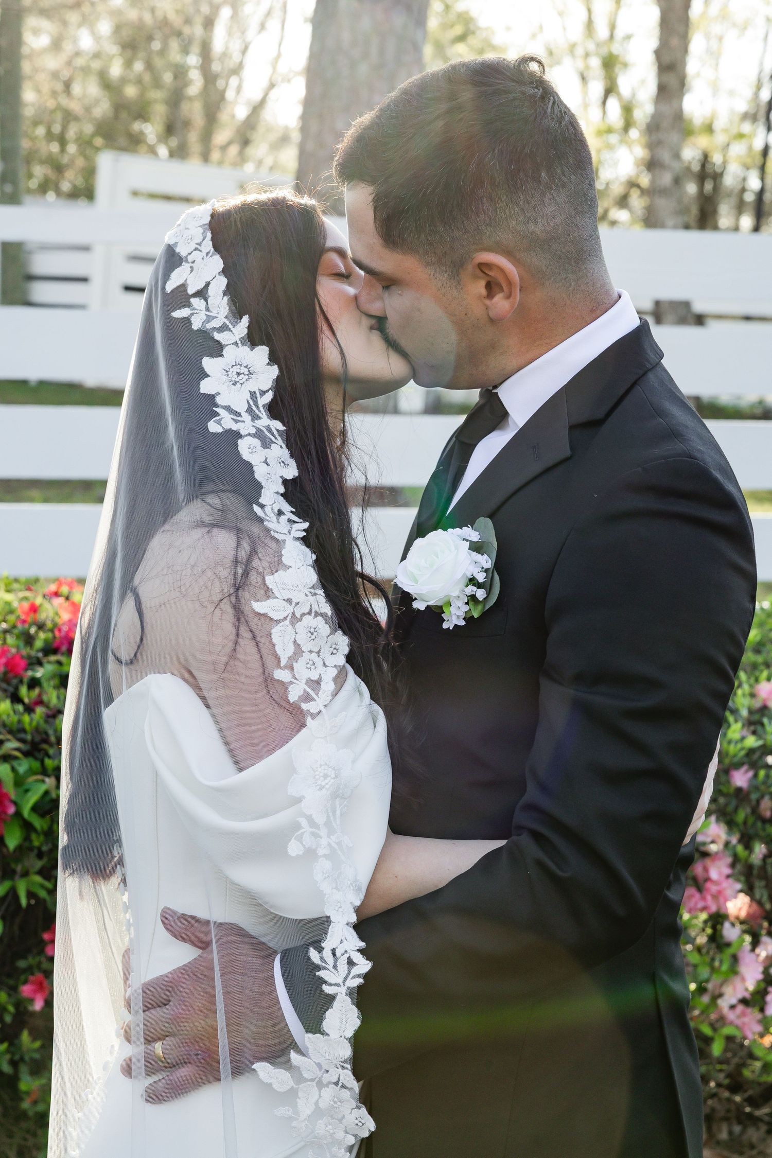 Newlywed couple shares a kiss outdoors with bride in lace veil and white gown.