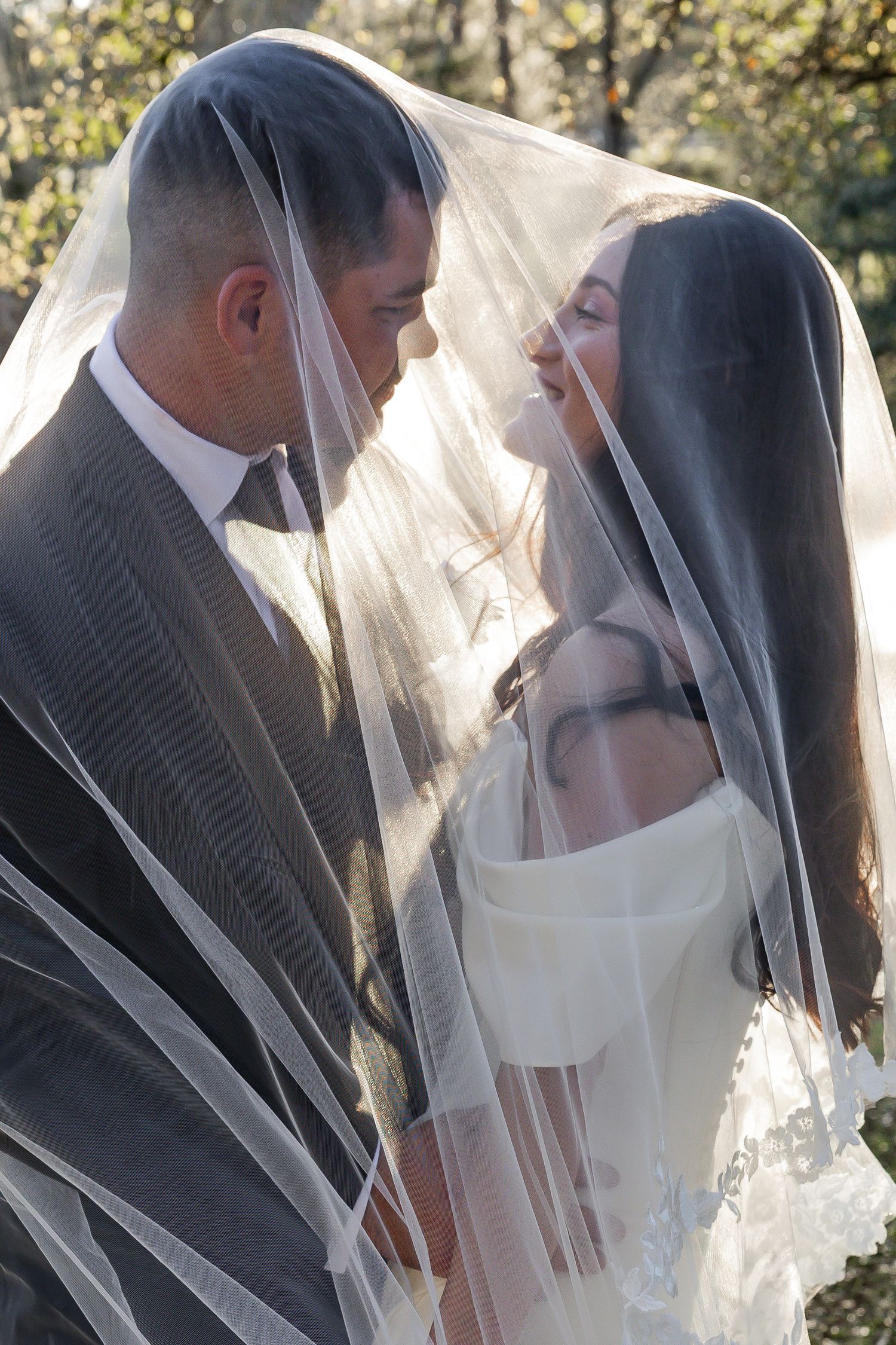Romantic bride and groom sharing an intimate moment under a sheer wedding veil outdoors.