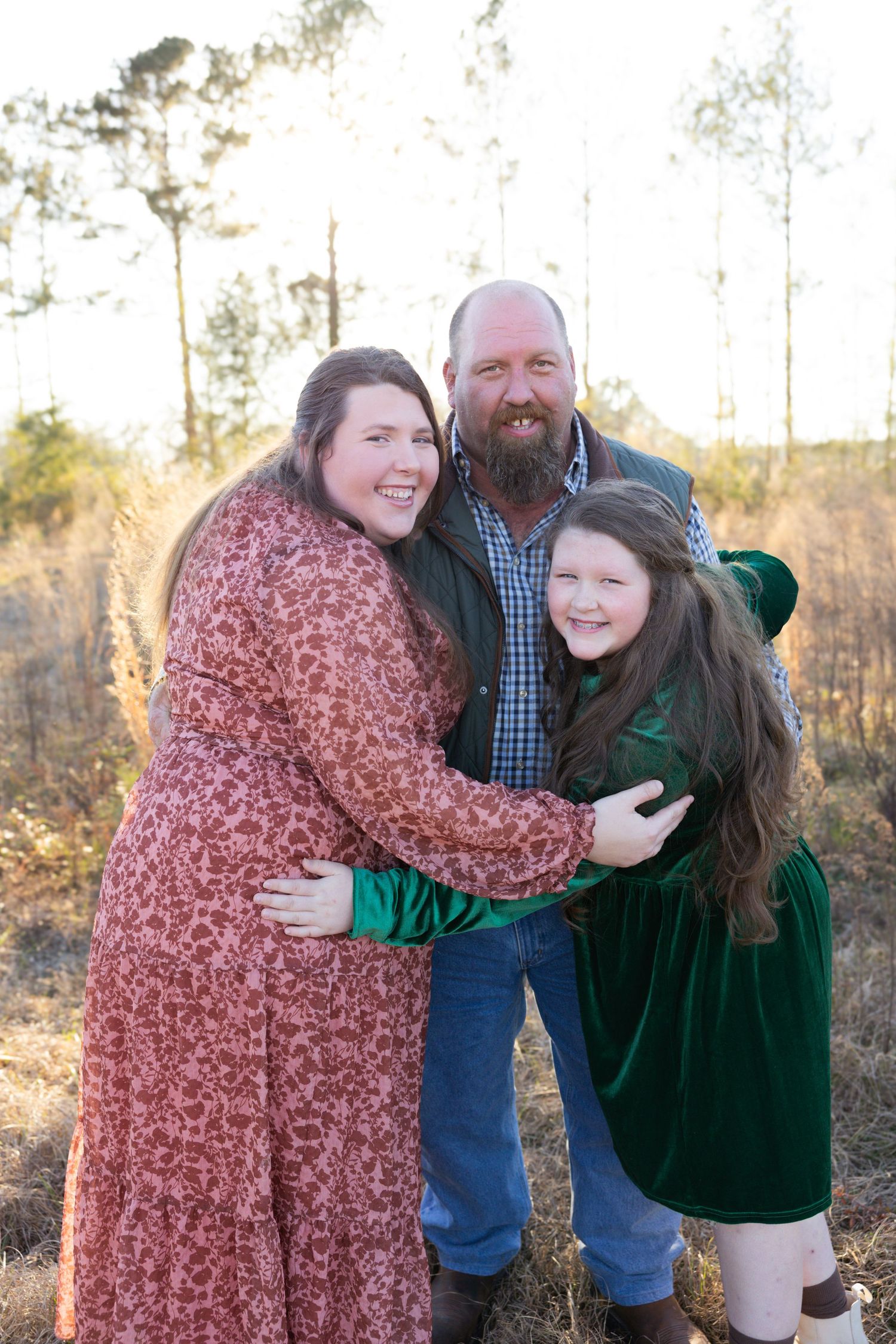 Father, mother, and young daughter sharing a warm embrace in a sunlit autumn field.