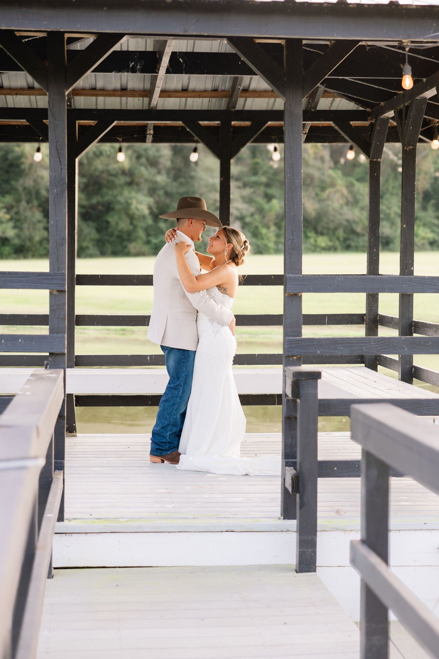 Bride and groom sharing a romantic kiss under a rustic wooden gazebo with string lights at an outdoor wedding venue. Wedding Photographer