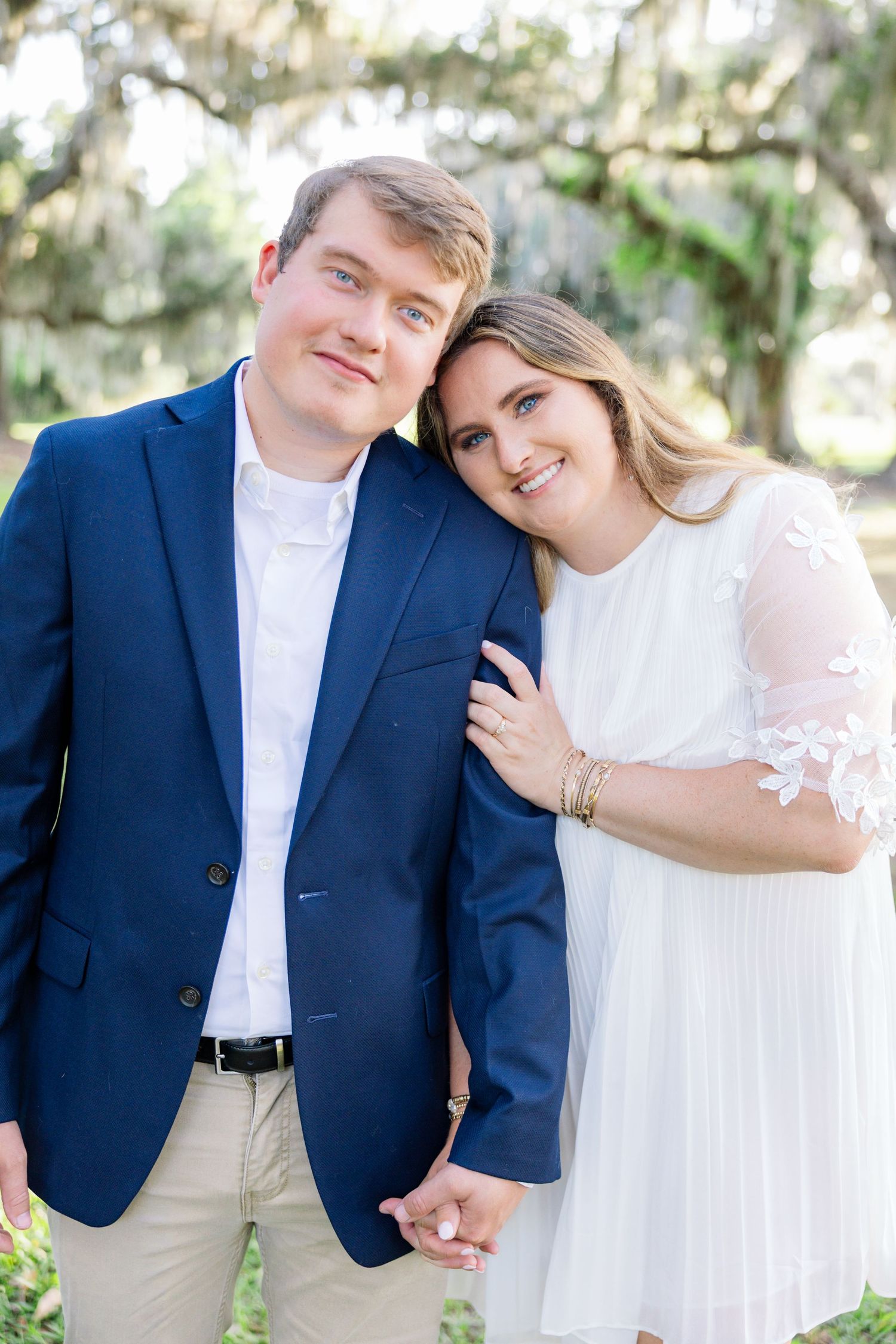 Joyful couple posing closely together outdoors under Spanish moss trees in natural light.