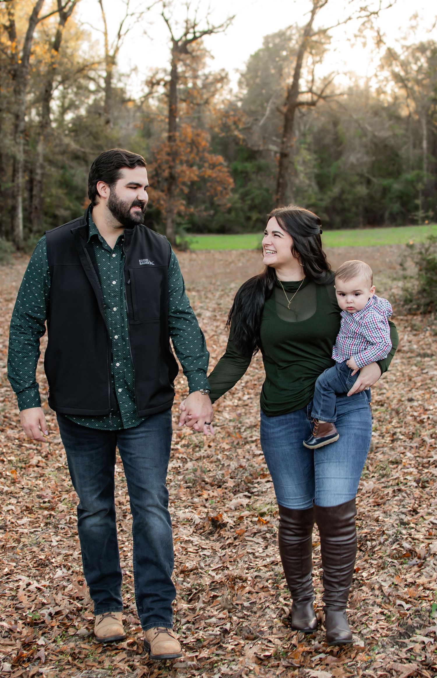 Happy couple holding hands walking with baby in fall leaves outdoor setting.