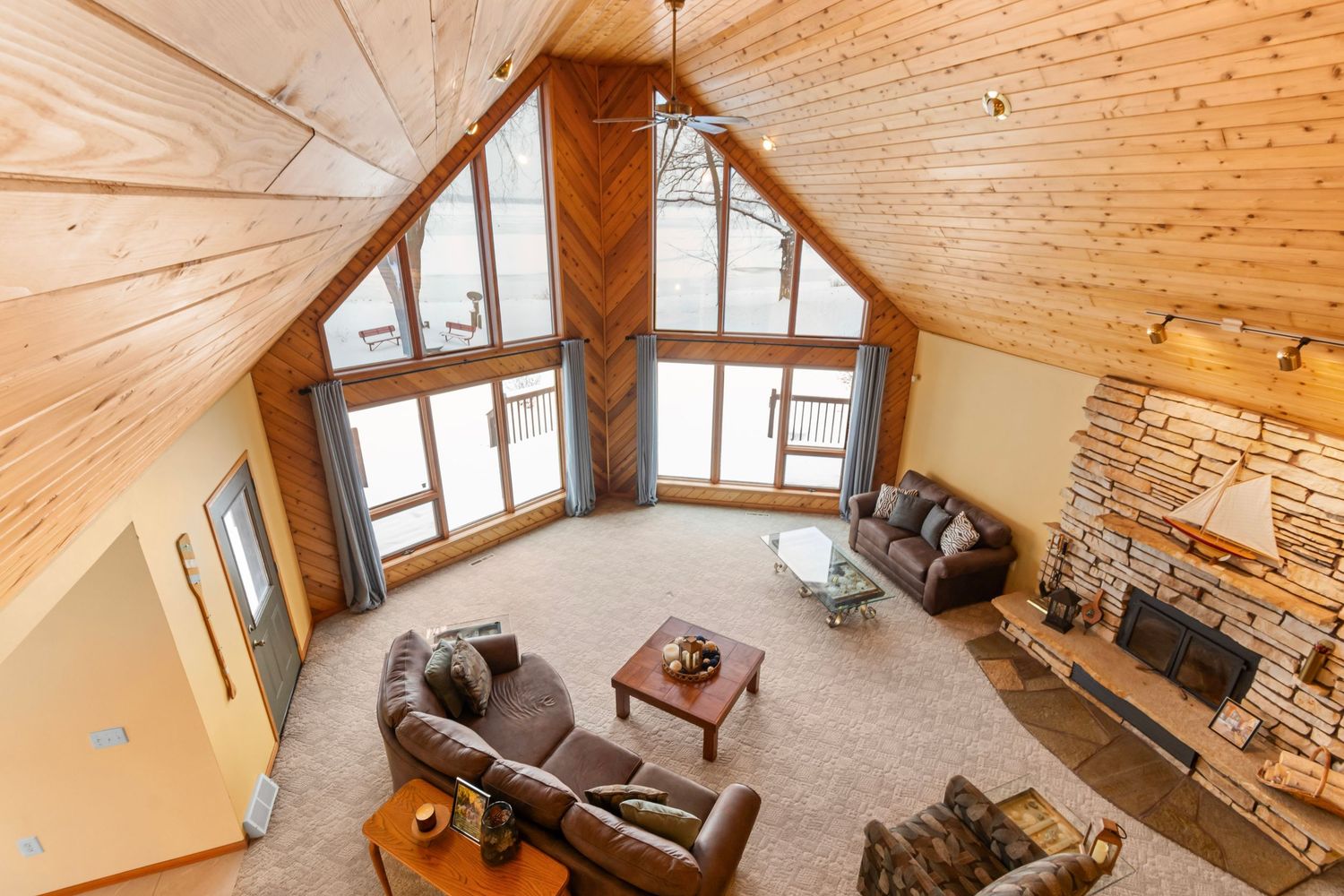 Open concept living room with cathedral ceiling, stone fireplace, and rustic wood beams.