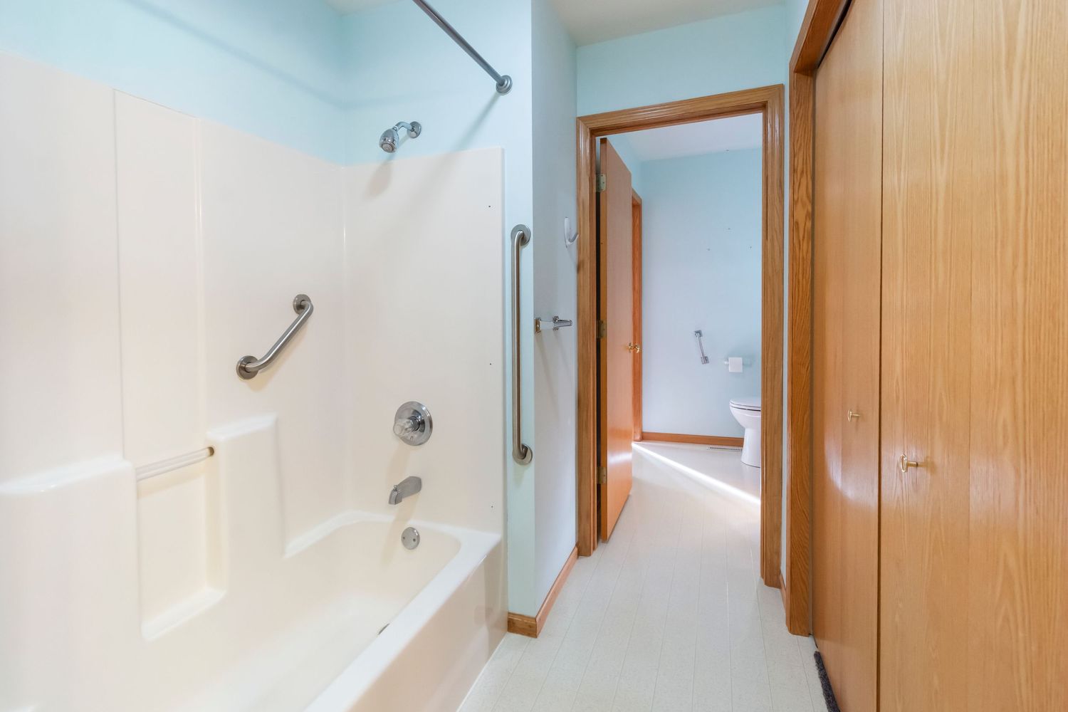 Modern bathroom with white bathtub, grab bars, and wooden door frames.