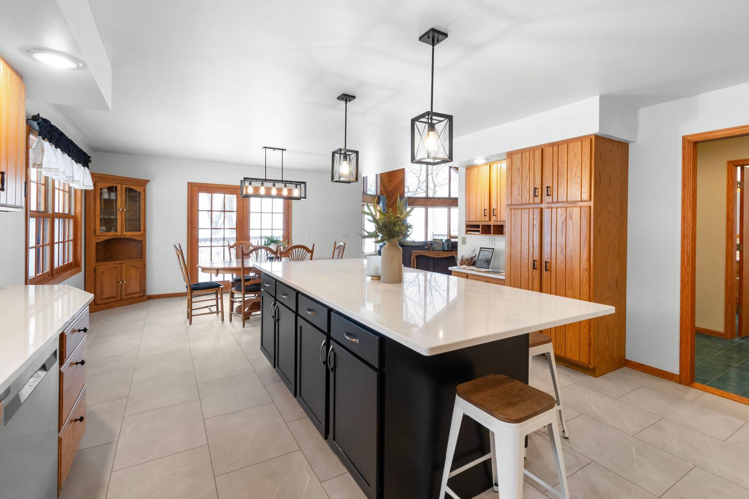 Open concept kitchen and dining area with modern black pendant lights and white counters.