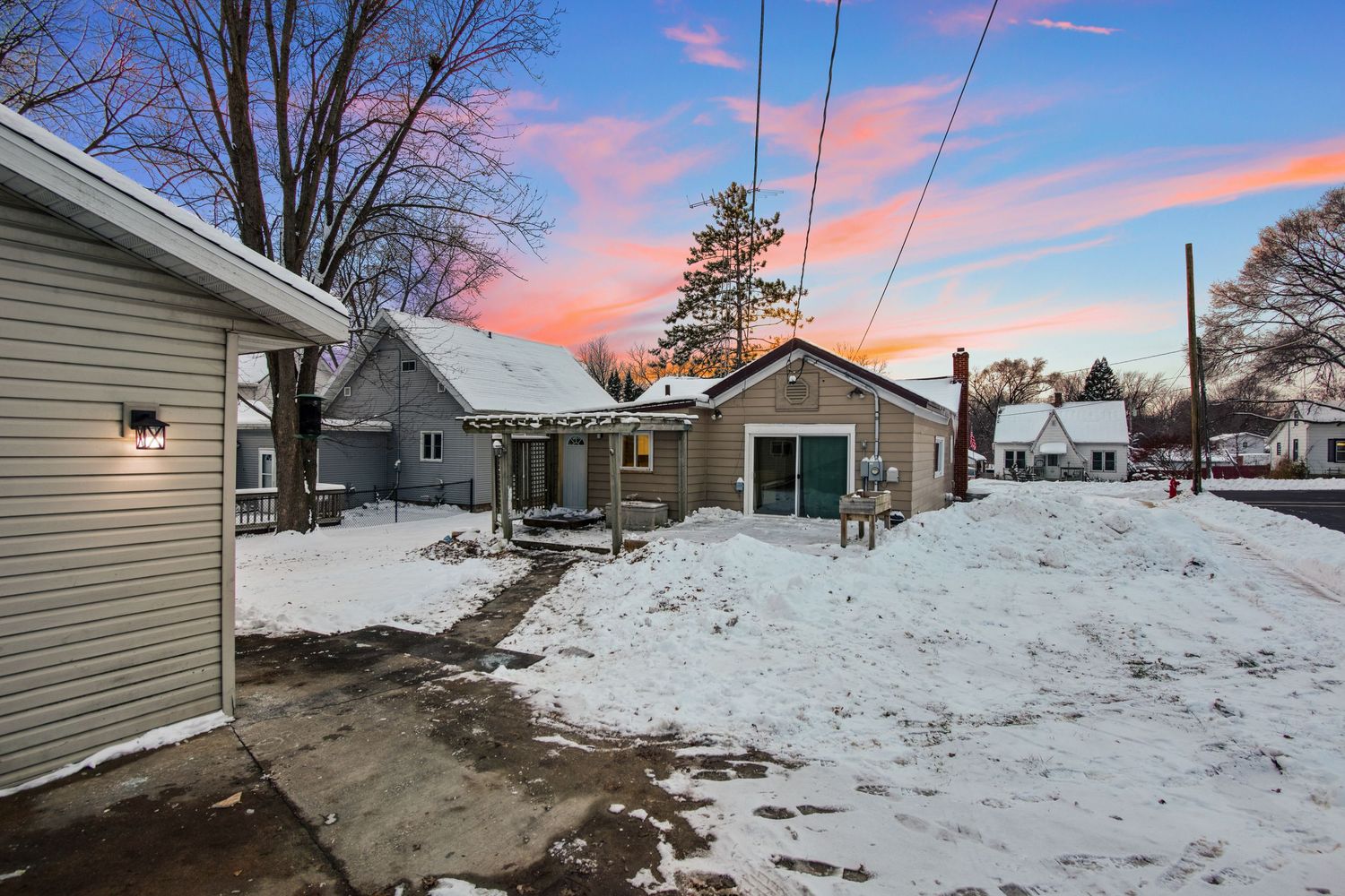 Snow covered property with power lines against pink sunset sky in winter.