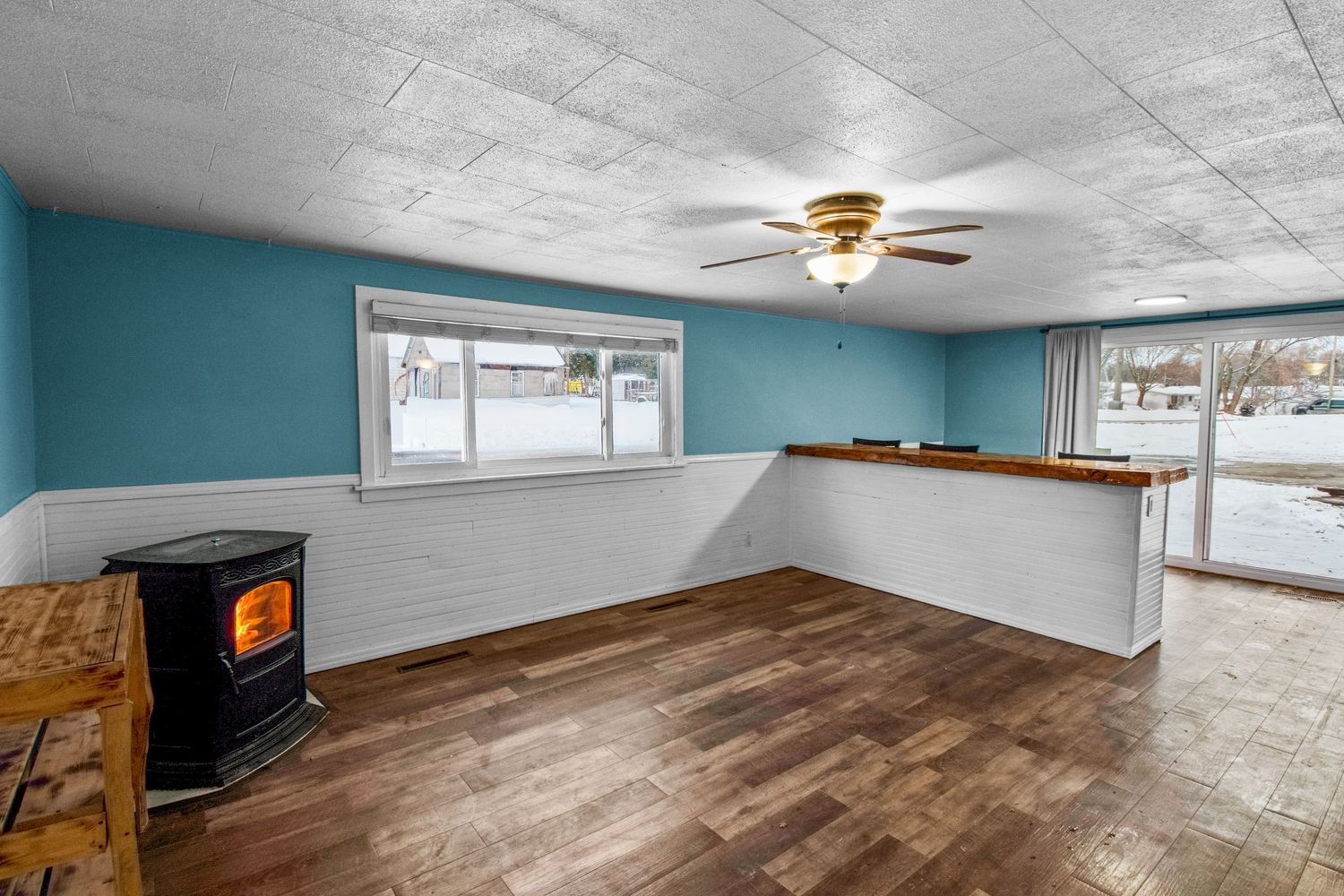 Spacious basement room with teal walls, ceiling fan, and newly installed hardwood flooring.