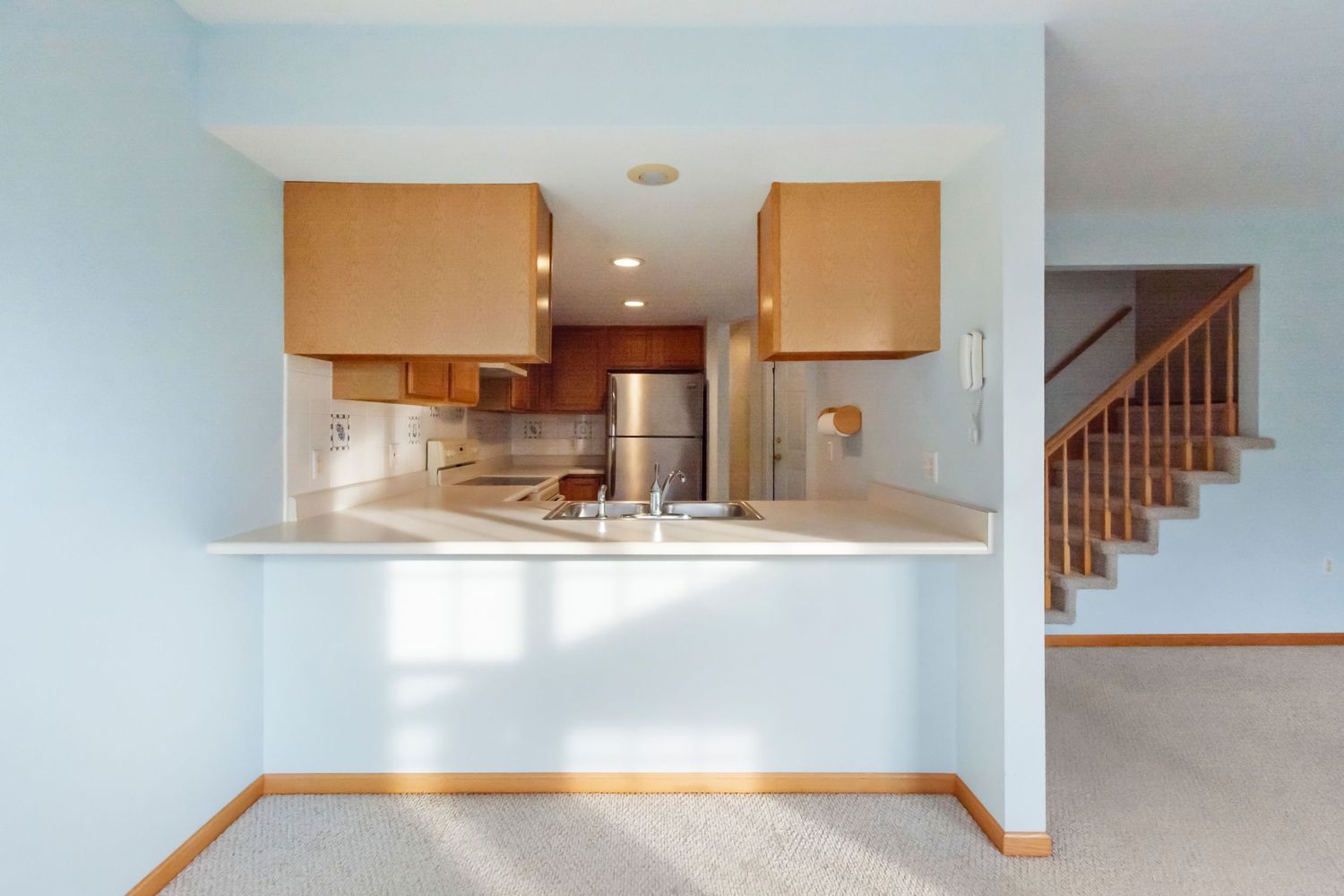 Open concept living area with beige walls and carpeted floors showing kitchen pass-through window.