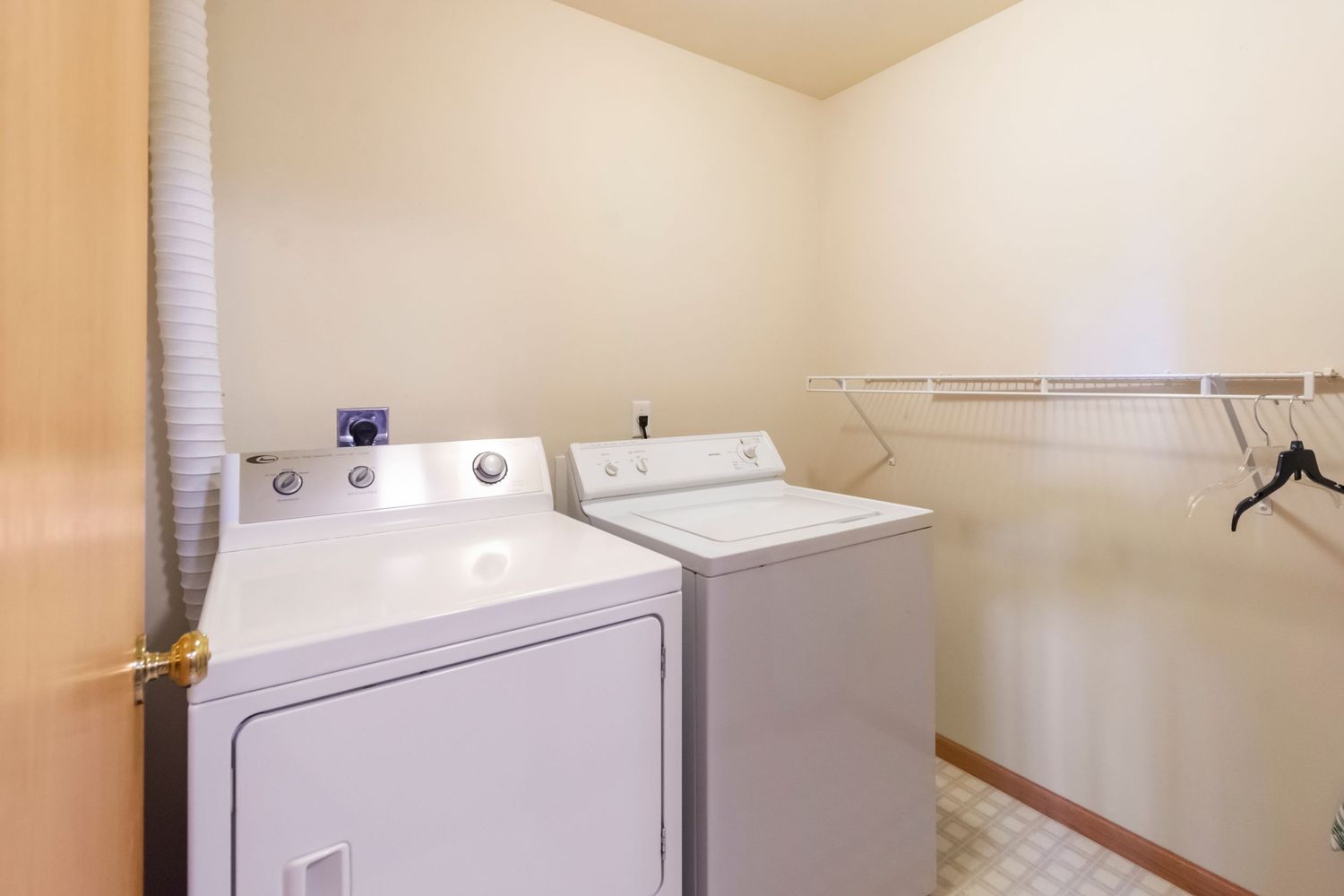 Laundry room with white washer and dryer units against cream colored walls and hanging storage rack.