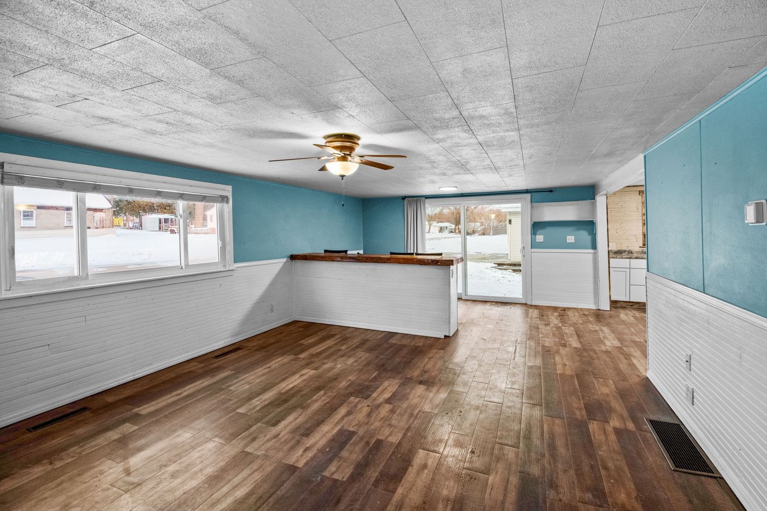 Spacious basement living area with textured ceiling, teal accent walls and rich hardwood floors.