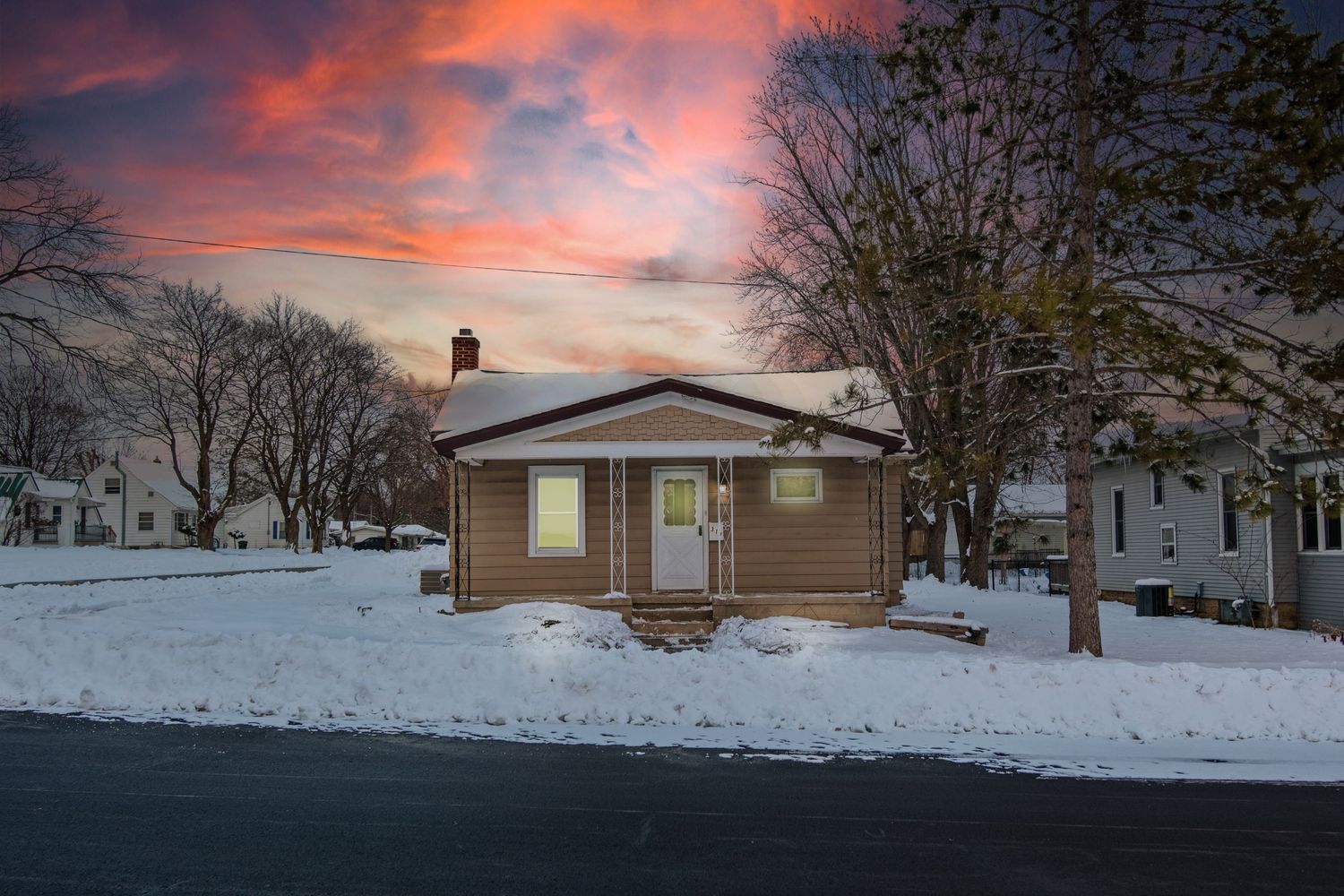 Row of snow-covered houses under a dramatic pink and orange winter sunset sky.
