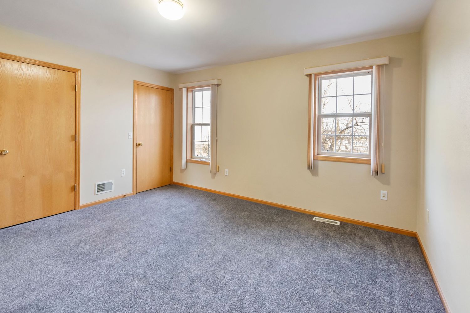 Bedroom with grey carpet, cream walls, and two windows with wooden trim.