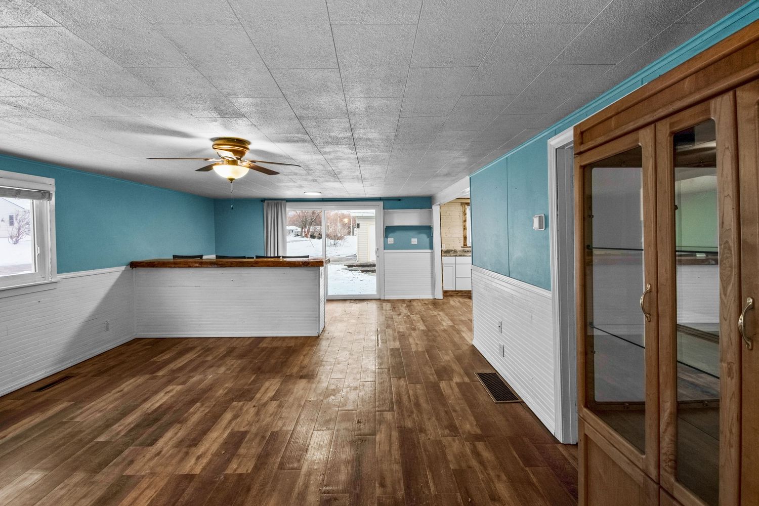 Multiple views of an unfurnished room with teal walls, wood flooring, and built-in display cabinets.