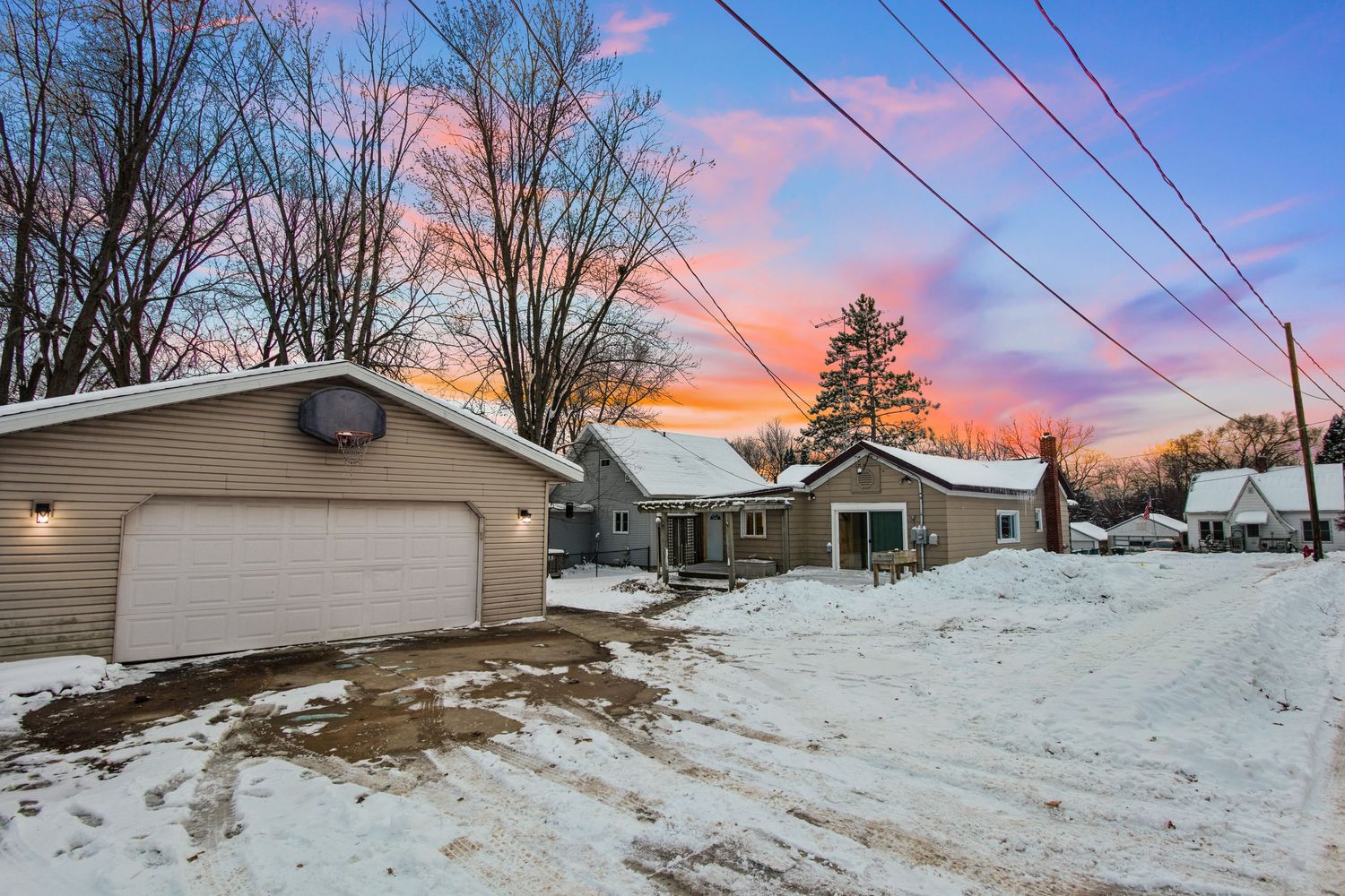 Residential home with attached garage captured during winter sunset with power lines overhead.