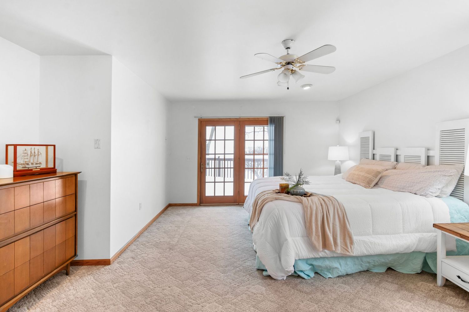 Airy bedroom with ceiling fan, white walls, and plush carpeting in neutral tones.