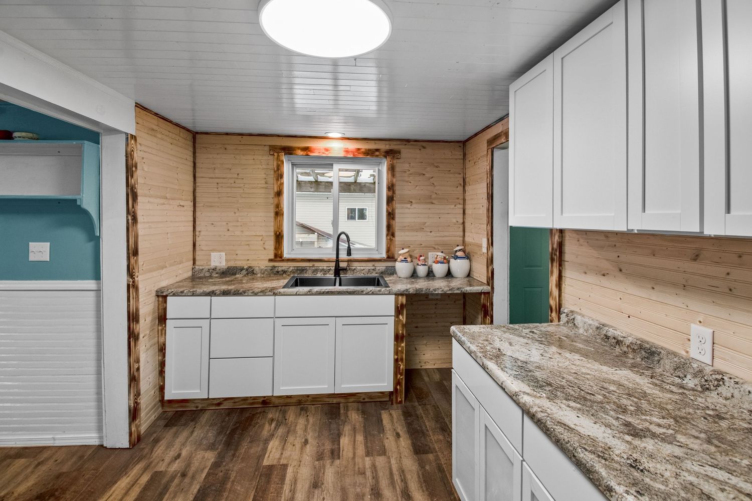 White kitchen cabinets with granite countertops and wood-look flooring in open concept layout.