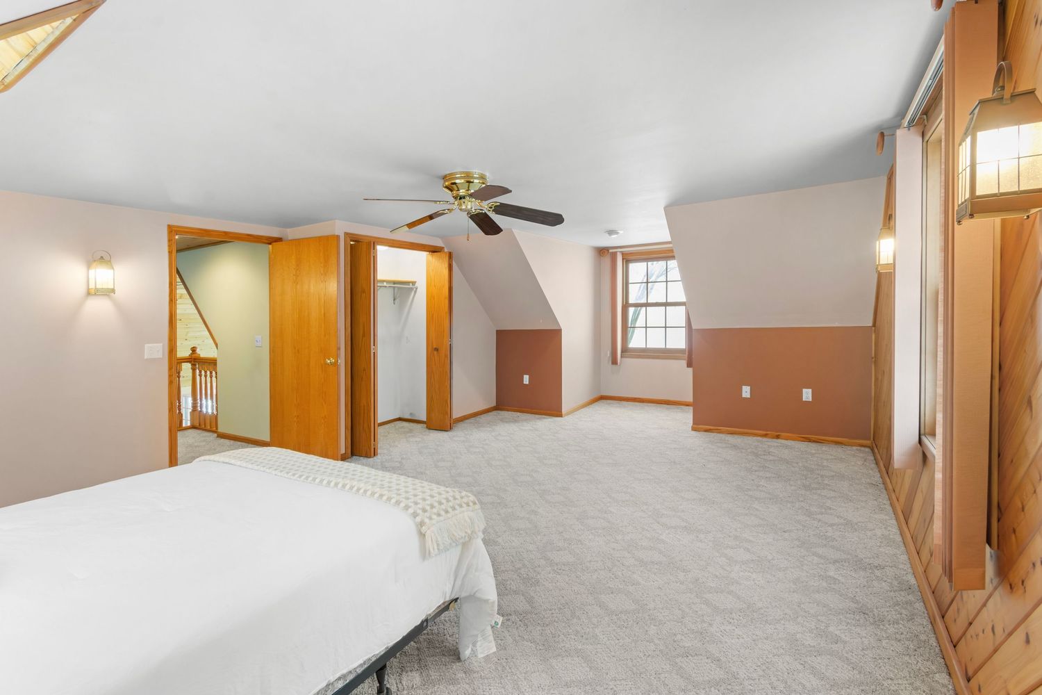 Spacious bedroom with sloped ceiling, carpeted floors, and wooden trim featuring ceiling fan and natural light.