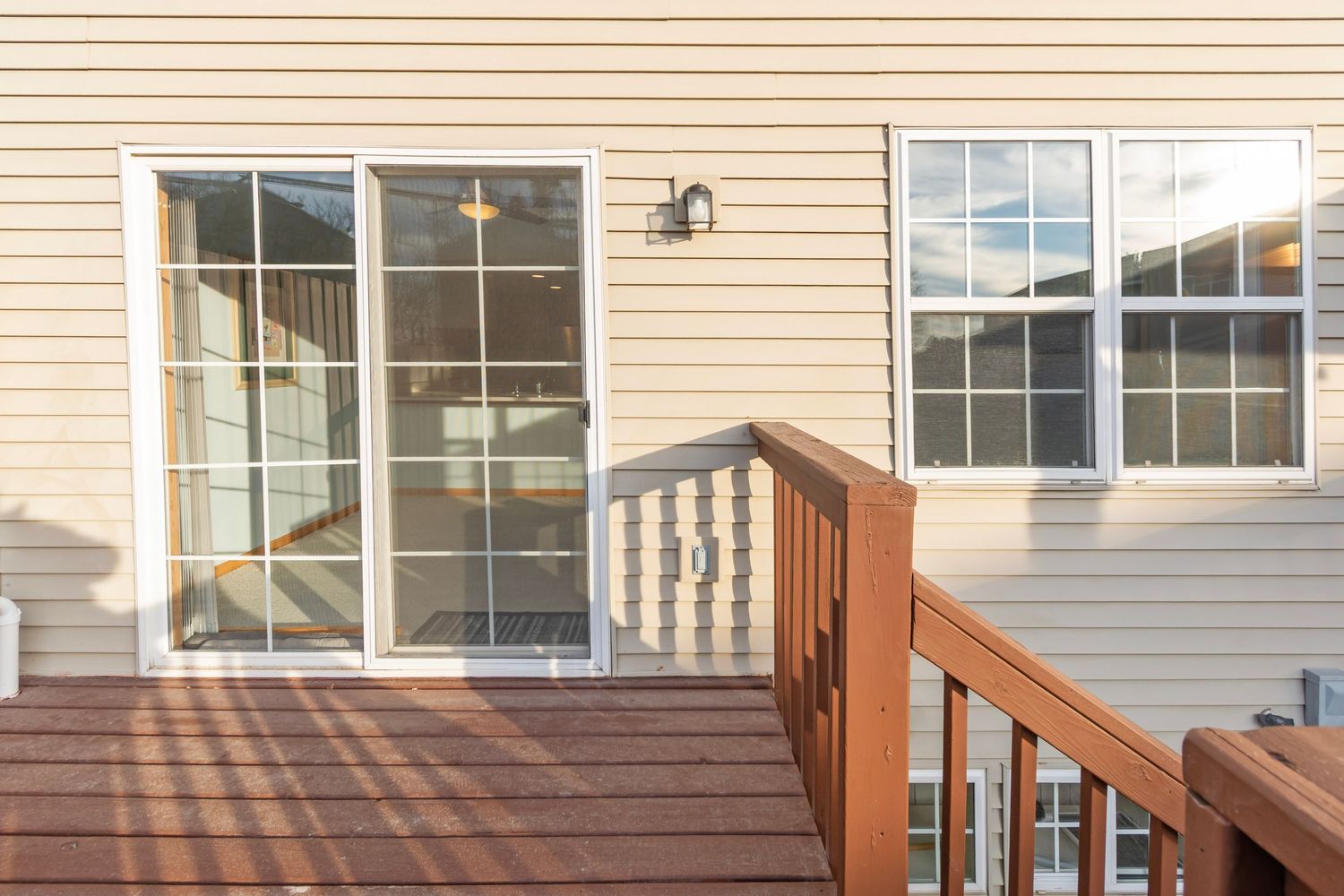 Back of beige house showing large windows and brown wooden deck railing.