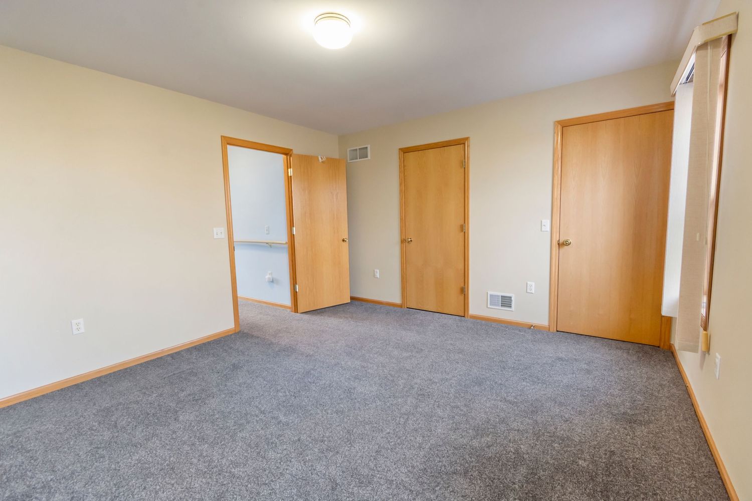 Empty bedroom with grey carpet, wooden doors, and cream colored walls.