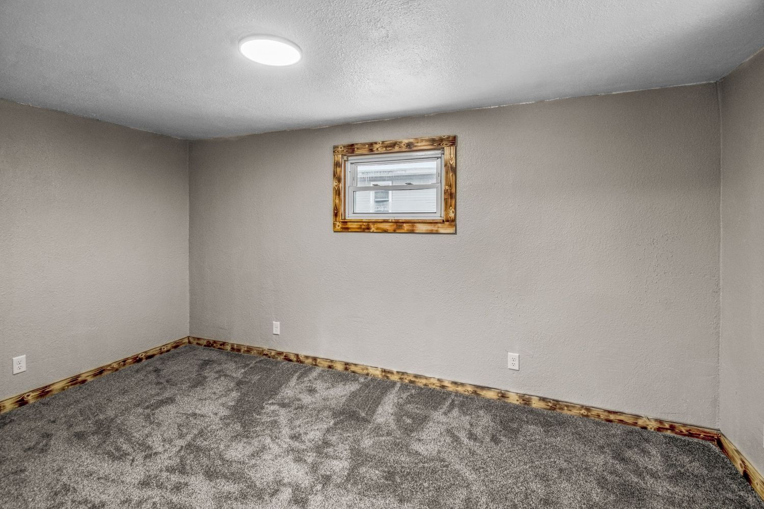 Empty basement room with gray carpet and rustic wood trim around windows.