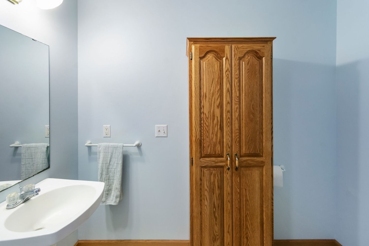Bathroom featuring blue walls, wooden storage cabinet, and white fixtures.
