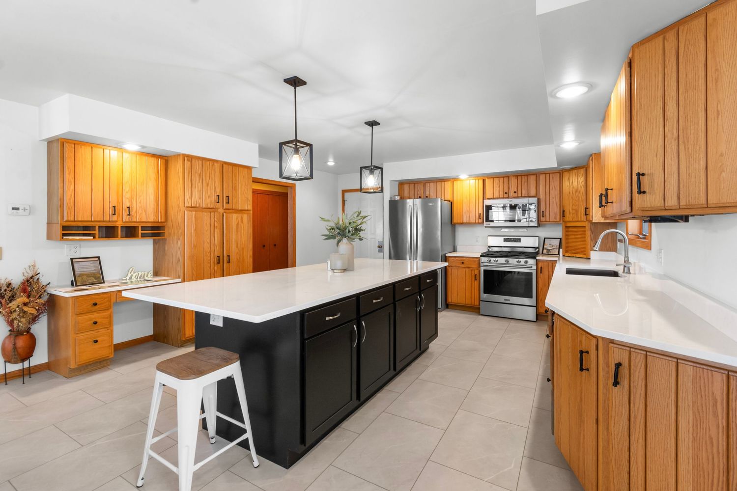 Modern kitchen with honey oak cabinets, black center island, white countertops and stainless steel appliances.