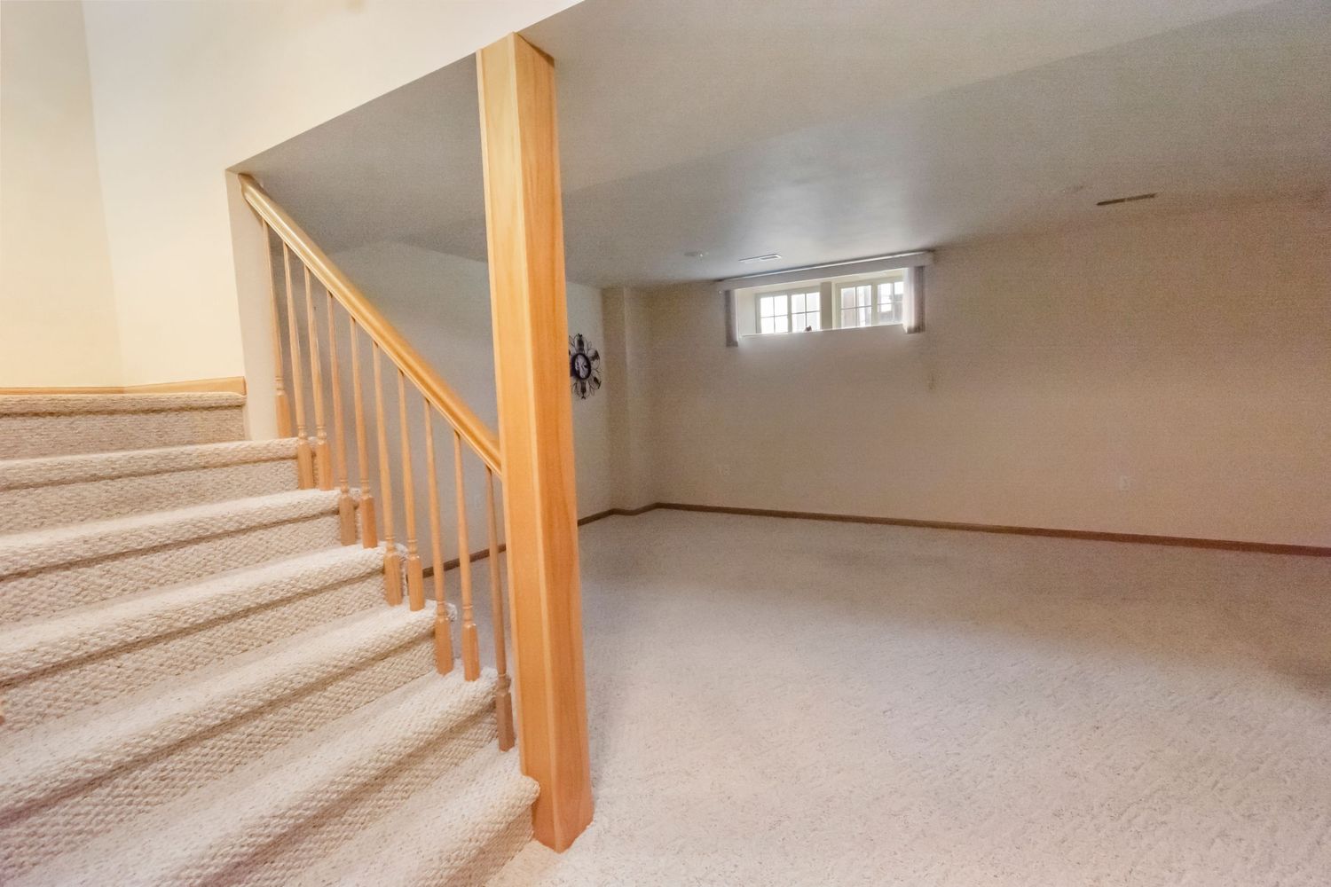 Carpeted basement stairs with wooden railing and beige walls in residential home.