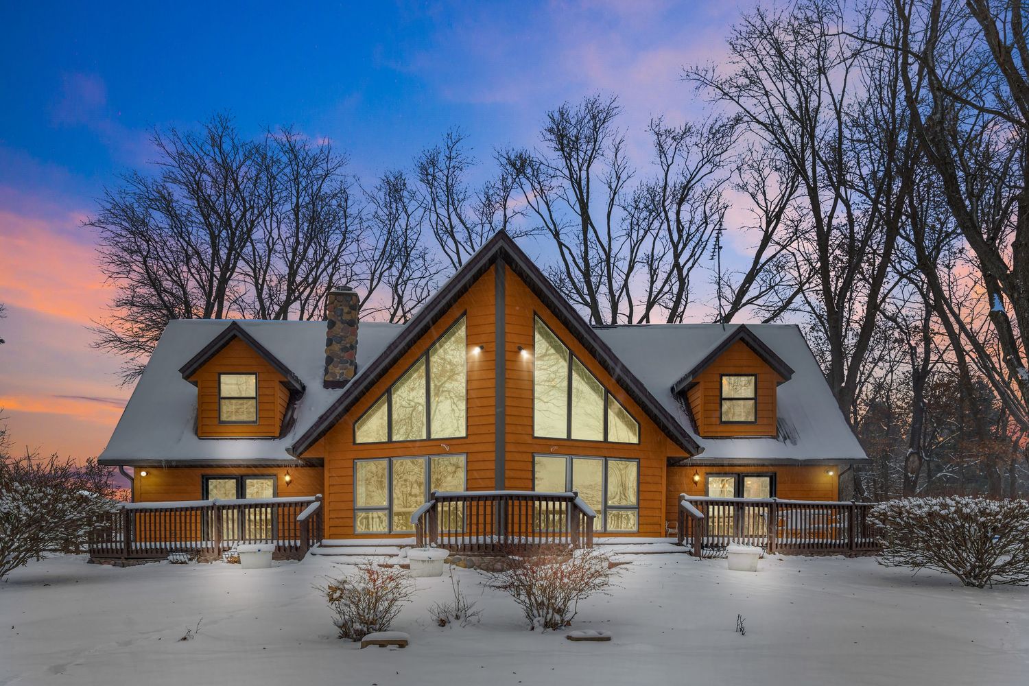 Sunset view of snow-covered rustic cabins with large windows and orange wood exterior.