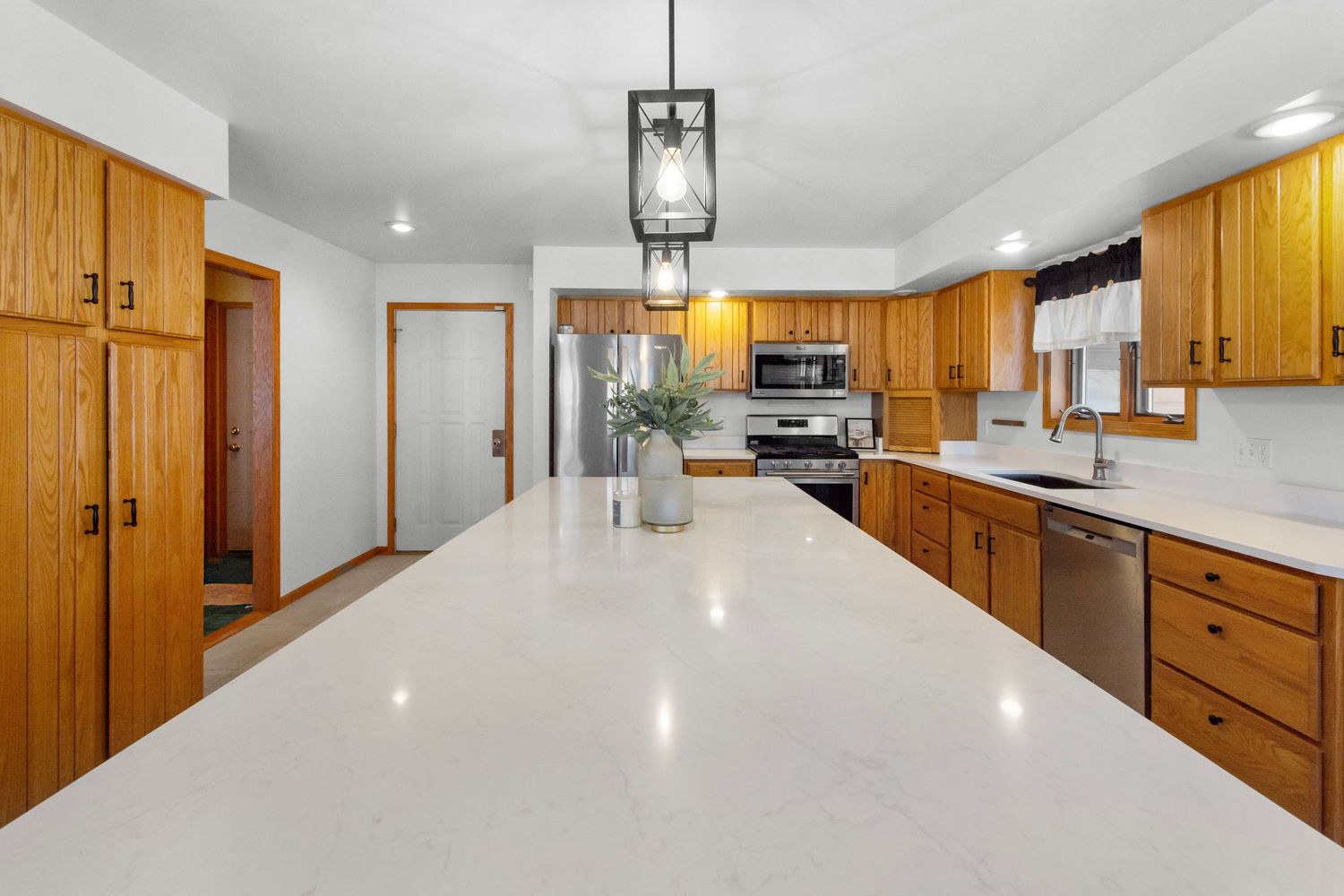 Long hallway view of modern kitchen with wooden cabinets and white countertops.