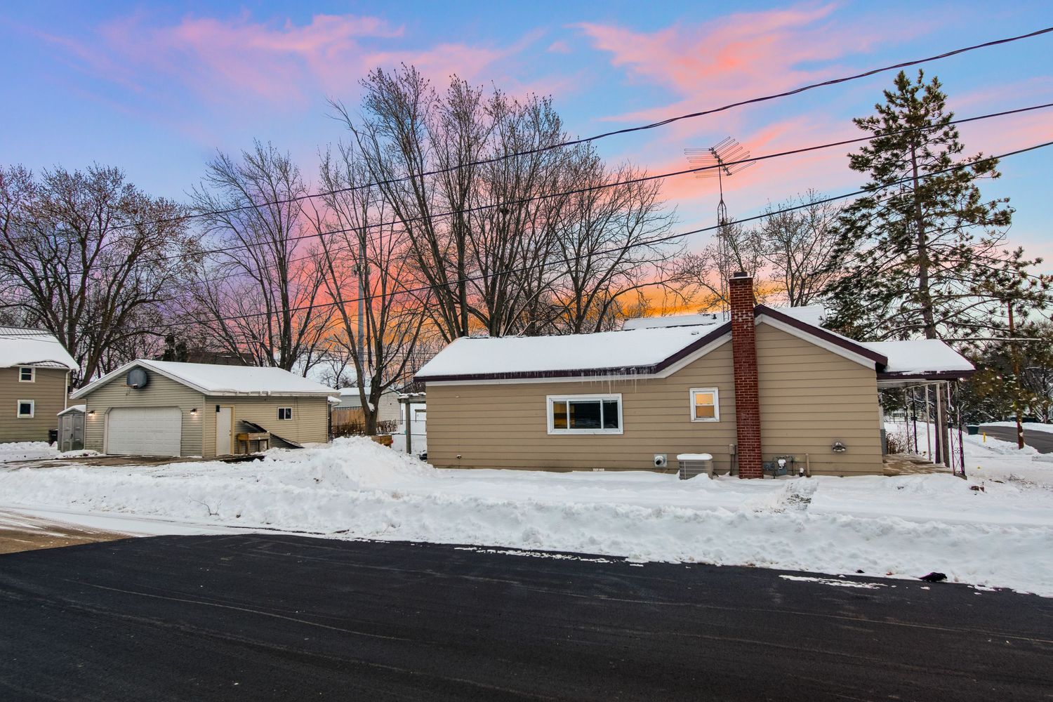 Small ranch house with attached garage in snowy setting during vibrant sunset.